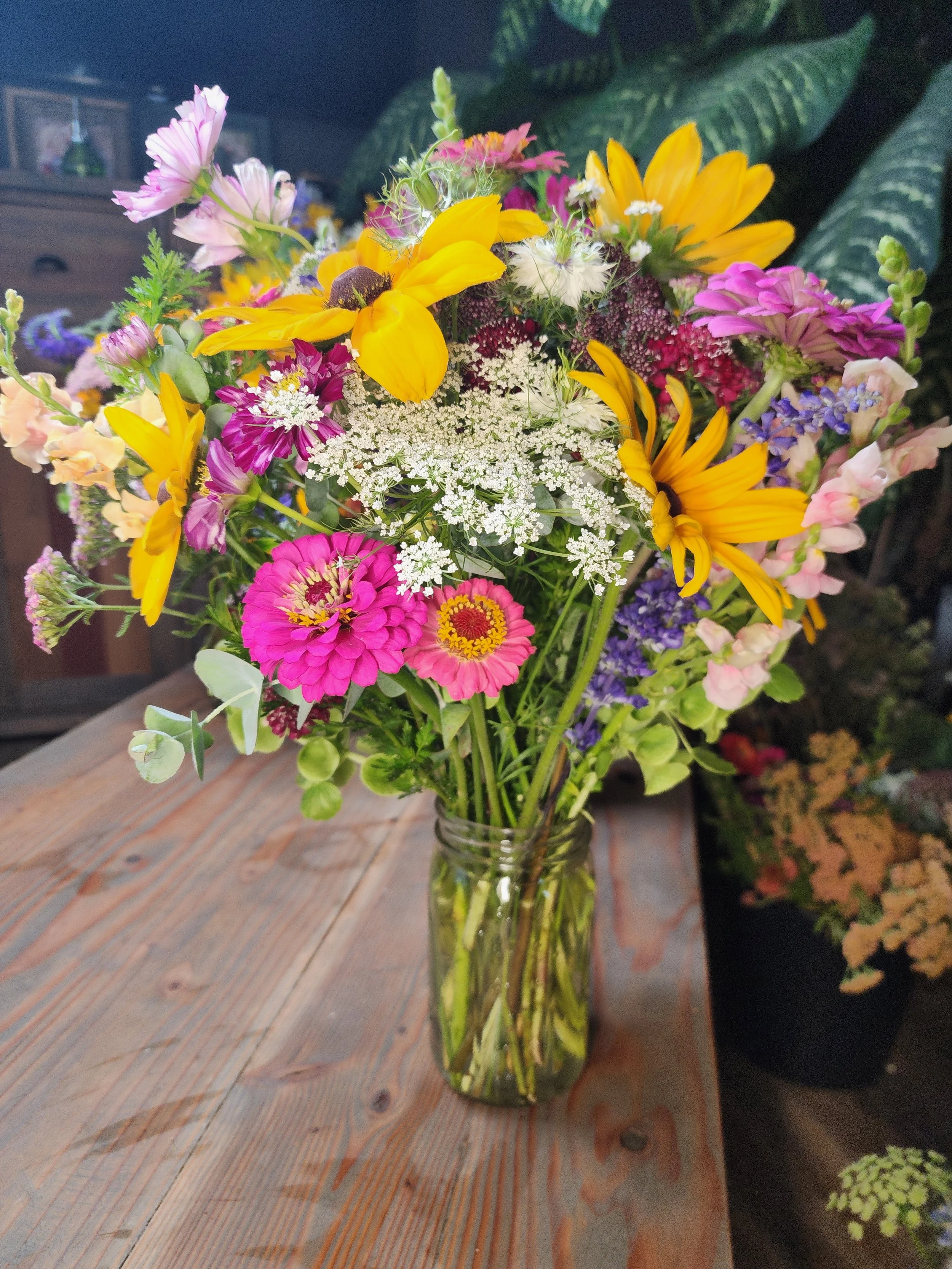 A colorful bouquet of various flowers in a clear glass vase on a wooden table.