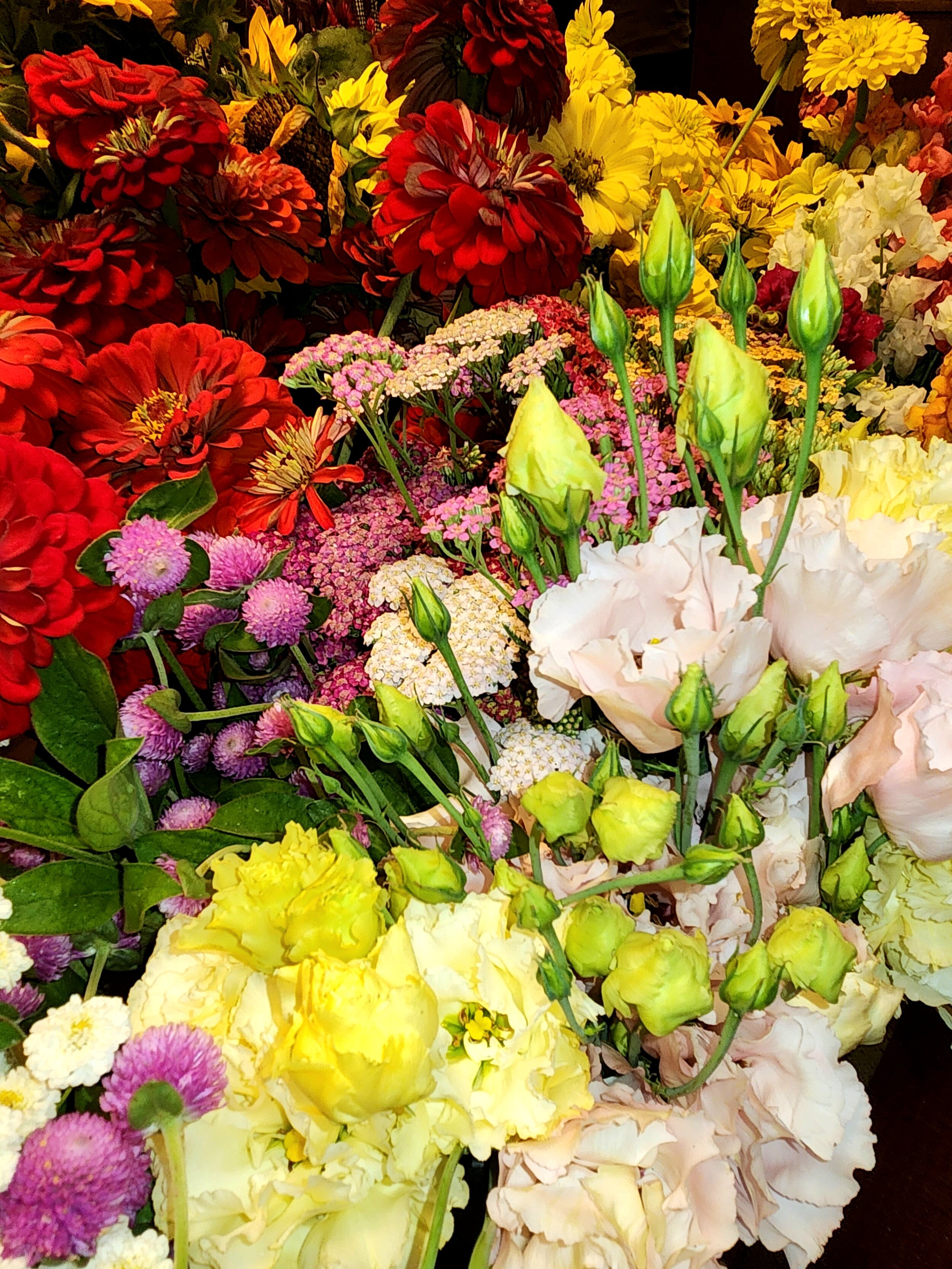 A vibrant assortment of various colorful flowers, including red dahlias, yellow carnations, white lisianthus, pink and purple asters, and other mixed blossoms.