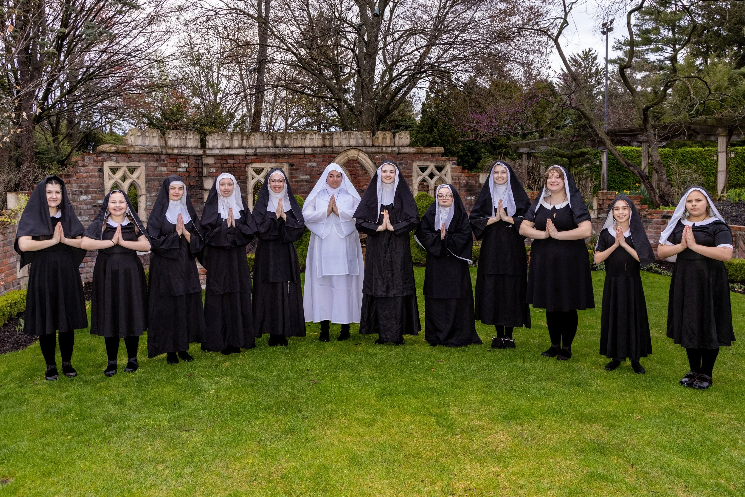 A group of girls dressed as nuns hold up praying hands