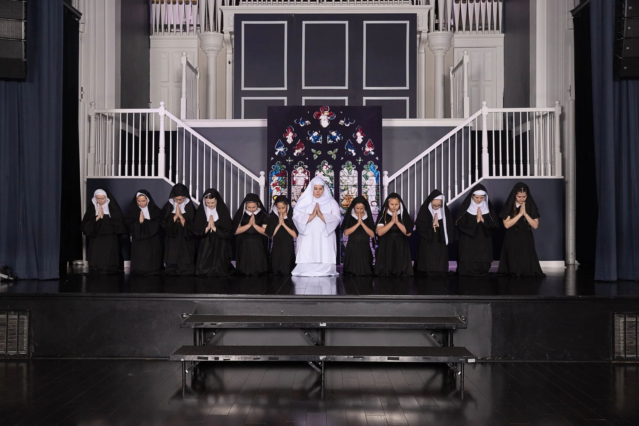Actors dressed as nuns kneel and pray