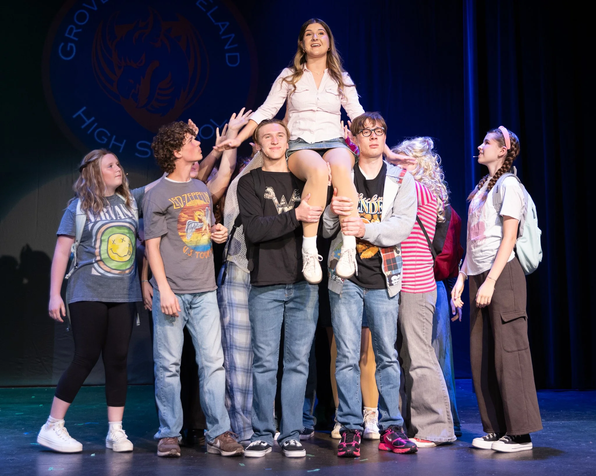 Two boys hold the actor playing Savannah on their shoulders while the rest of the cast, clumped behind them, gesture and look to her in admiration