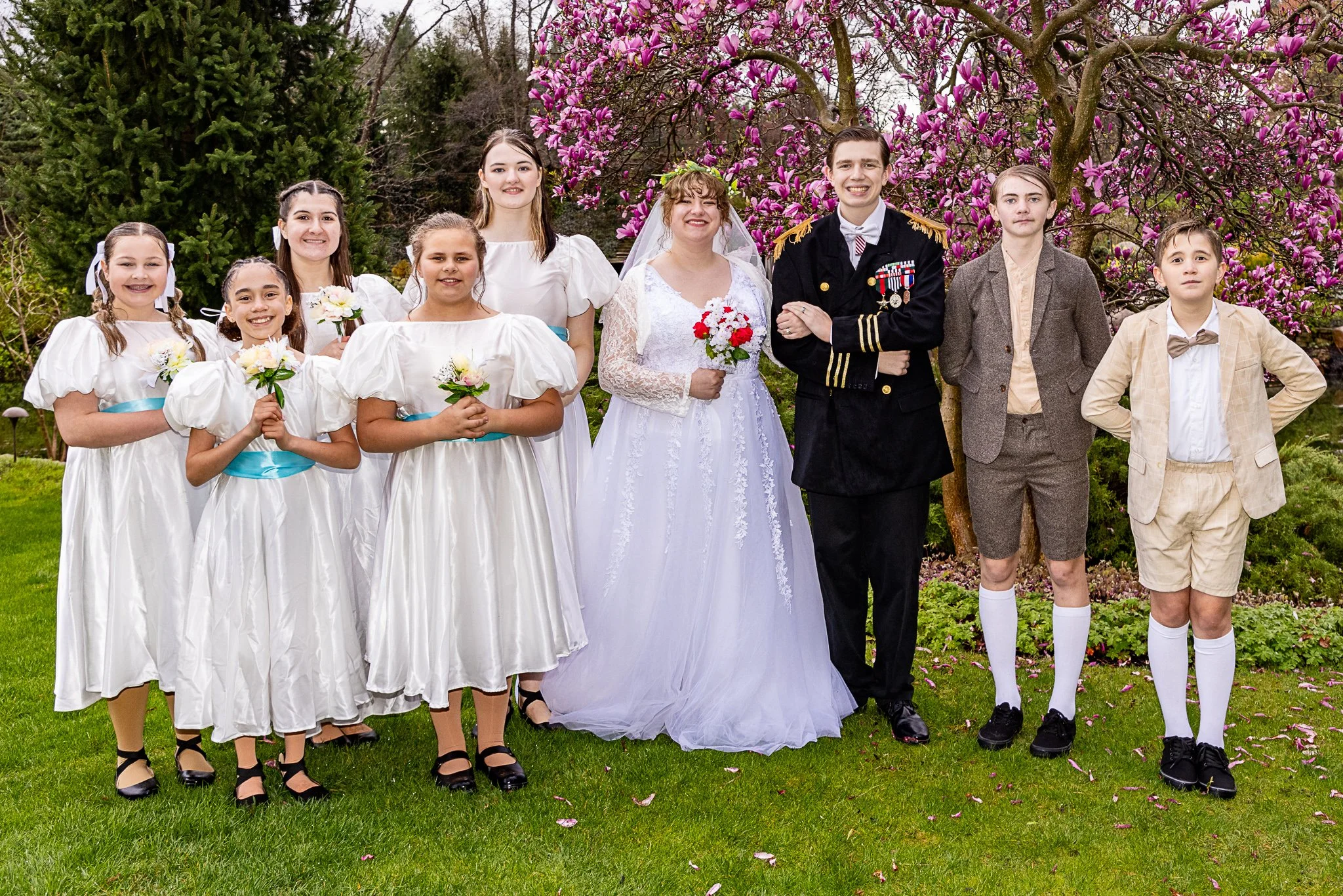 Nine actors dressed as if for a wedding smile