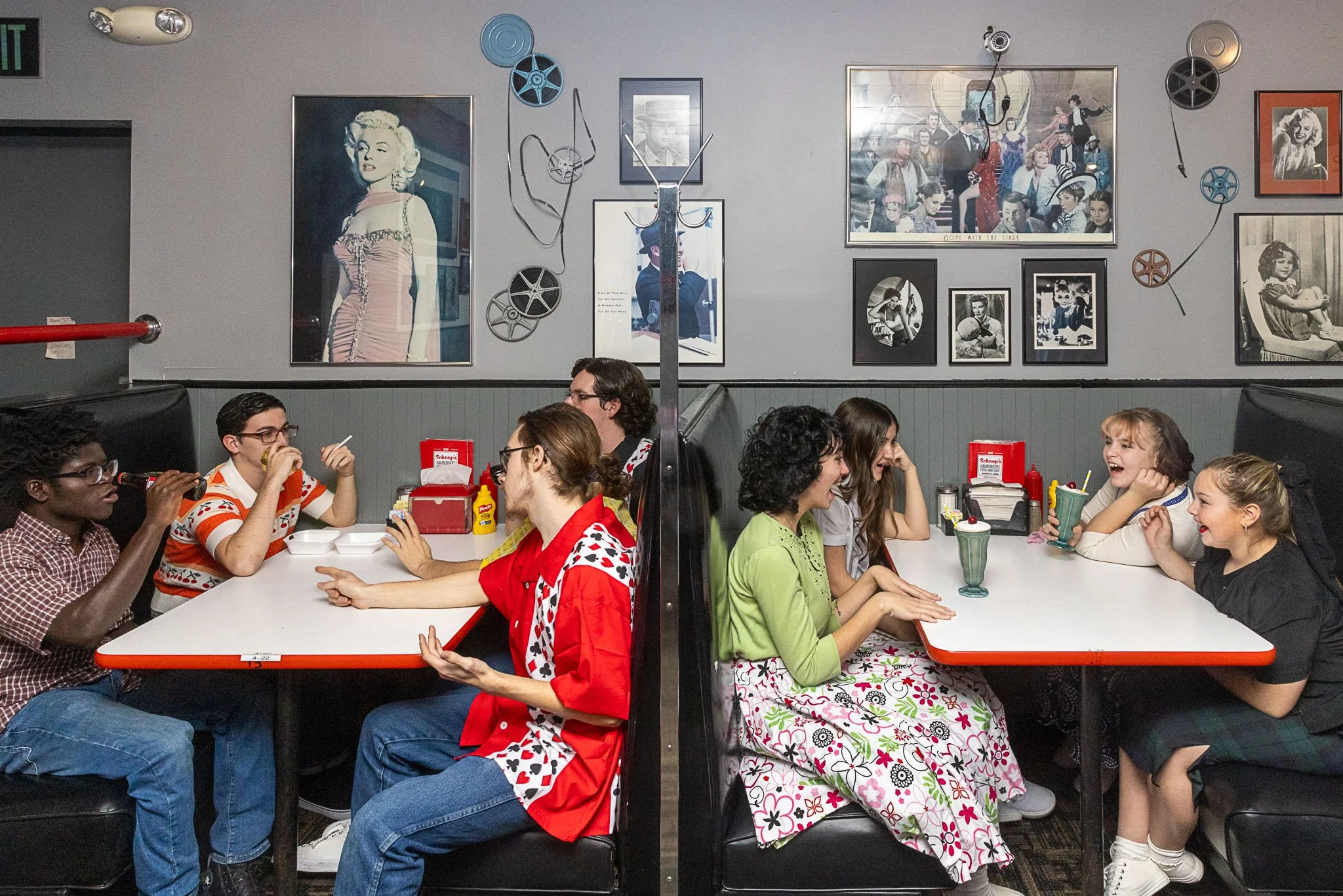 Two booths, one of boys and one of girls, sit and talk to one another in a restaurant