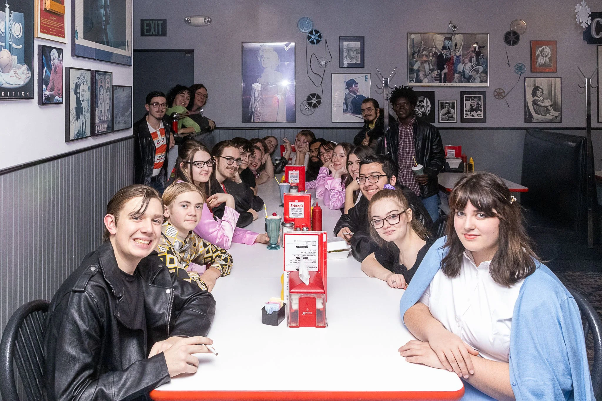 The cast of Grease sits in a restaurant together and smiles
