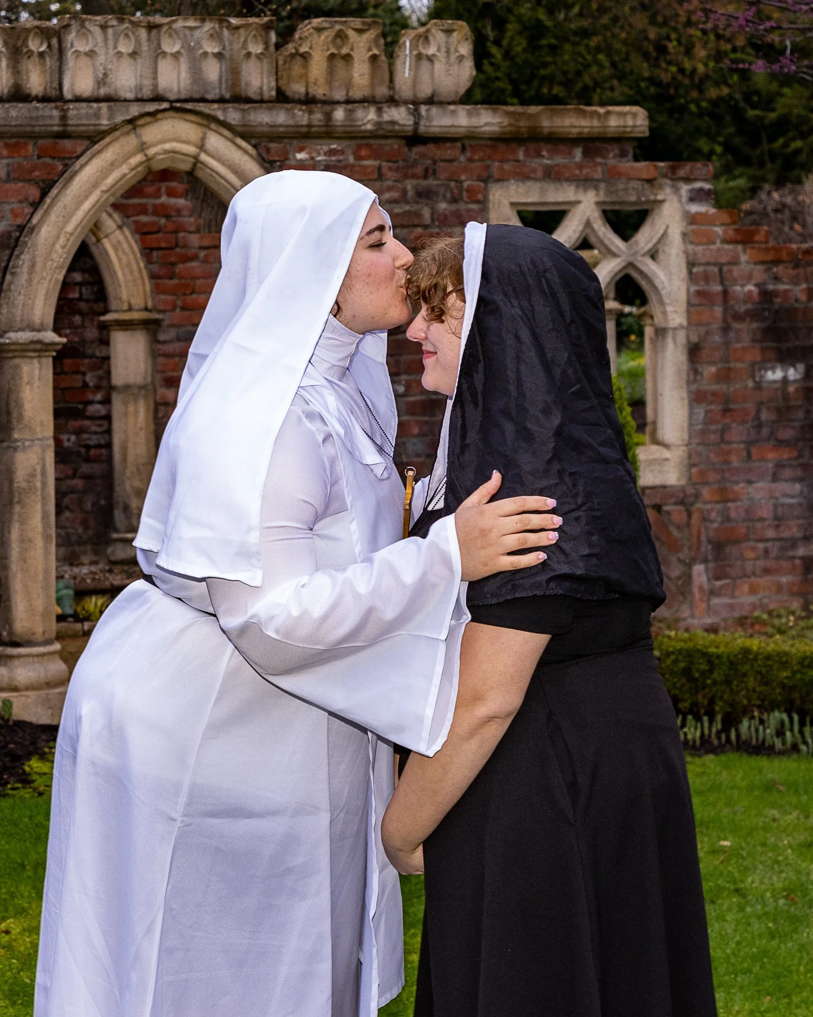 An actor wearing a nun costume kisses another actor on the forehead