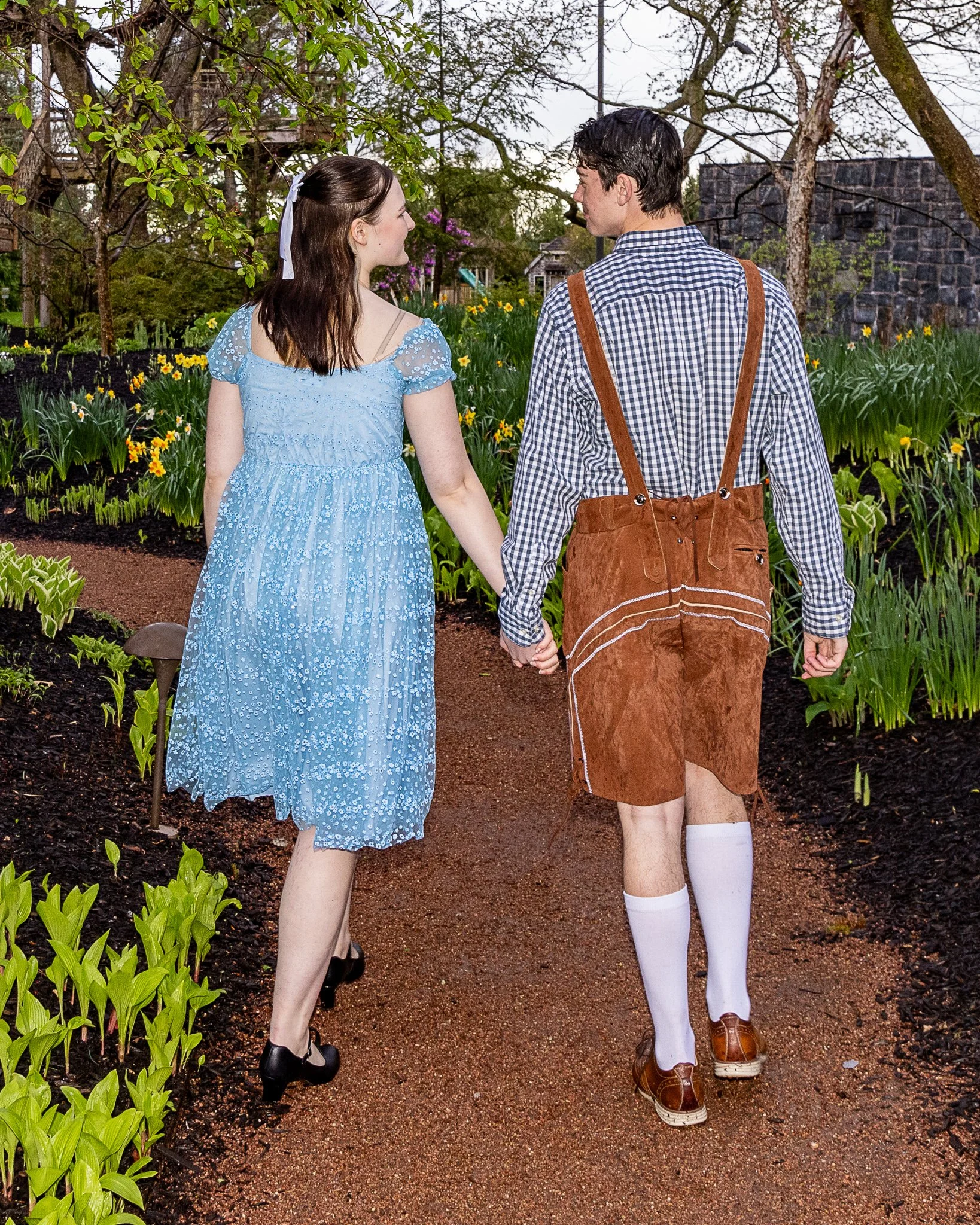Two actors walk away from the camera and hold hands