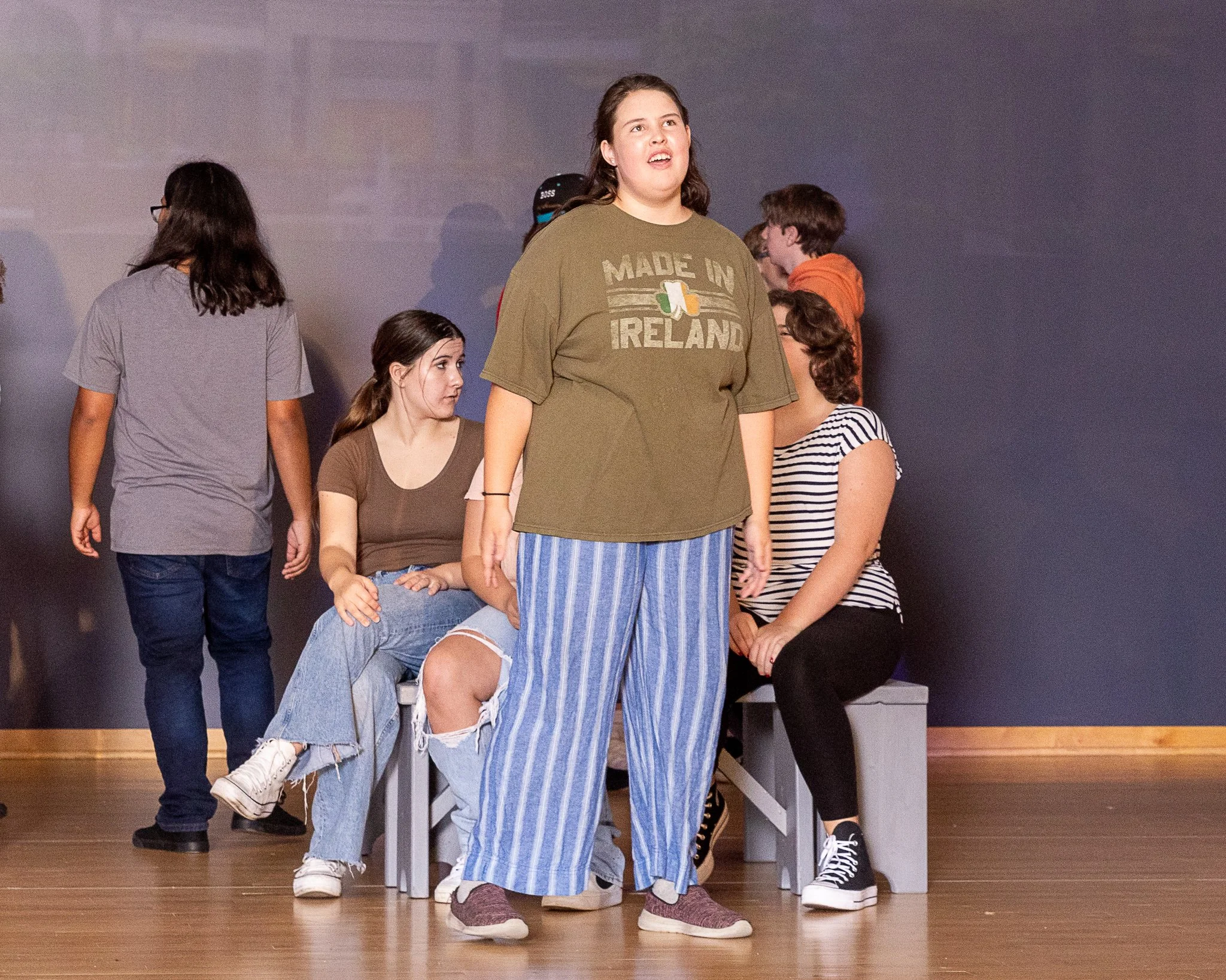 An actor sings as other actors sit behind her