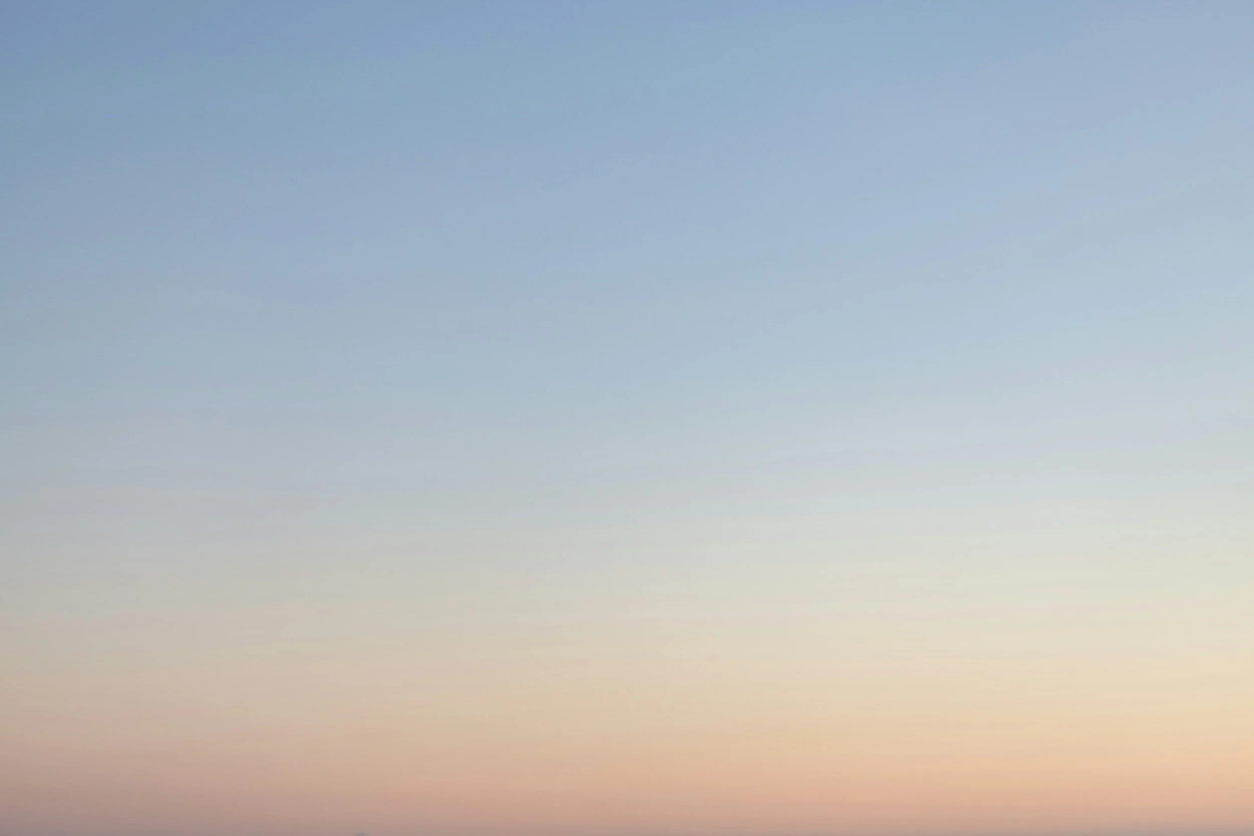 A smiling woman with reddish hair, wearing blue medical scrubs and multiple necklaces and earrings, standing against a plain white wall.