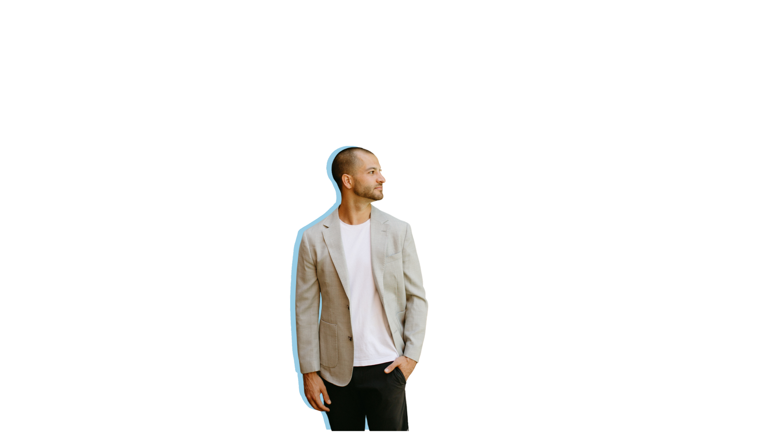 A man wearing a beige blazer and black pants standing with his hands in his pockets, looking to his left.