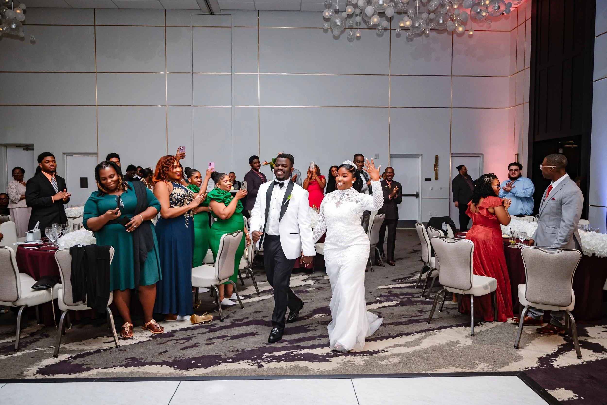A wedding reception with a bride and groom dancing, surrounded by guests taking photos and clapping.
