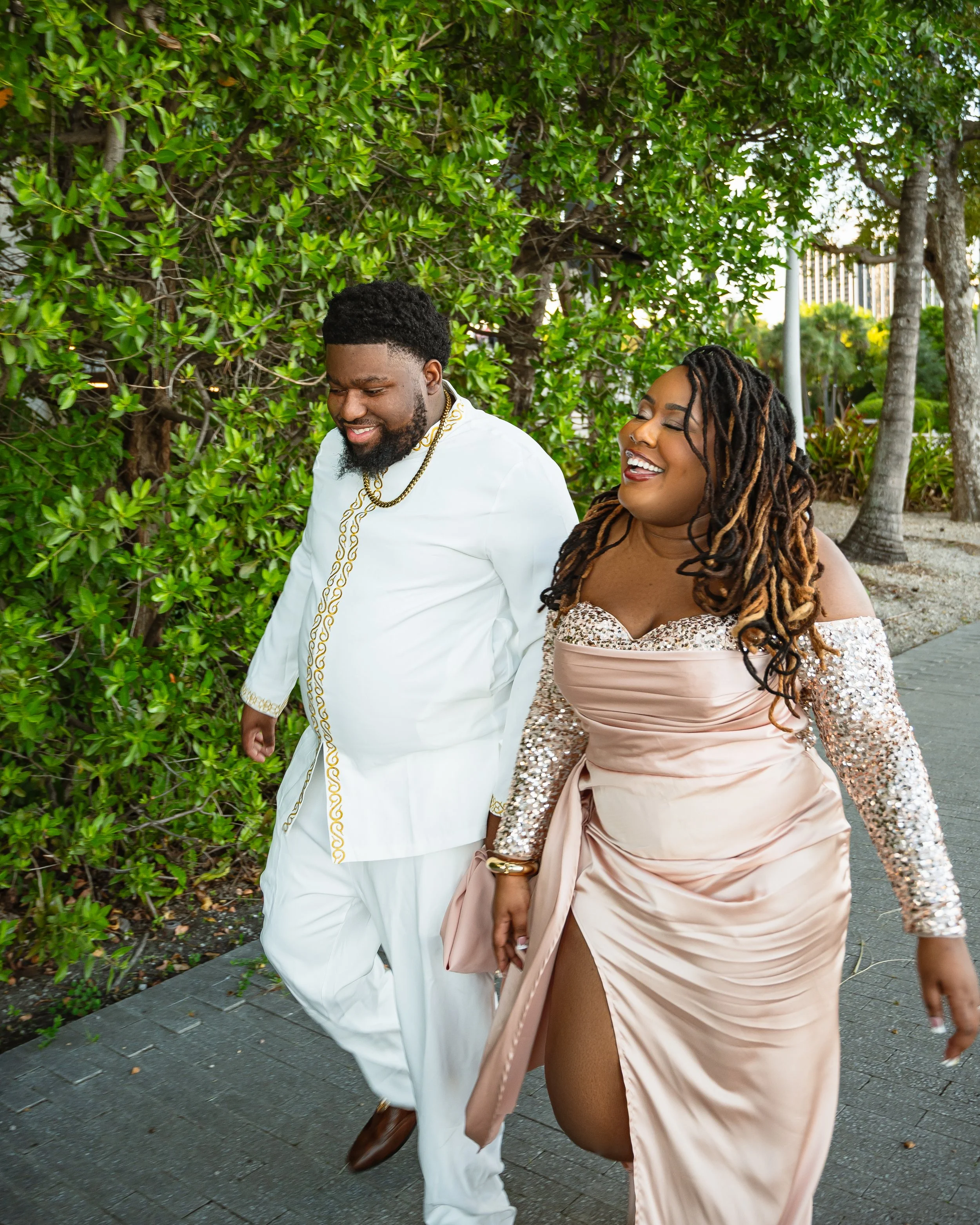 A man and woman walking together outdoors, both dressed elegantly, smiling and enjoying each other's company.