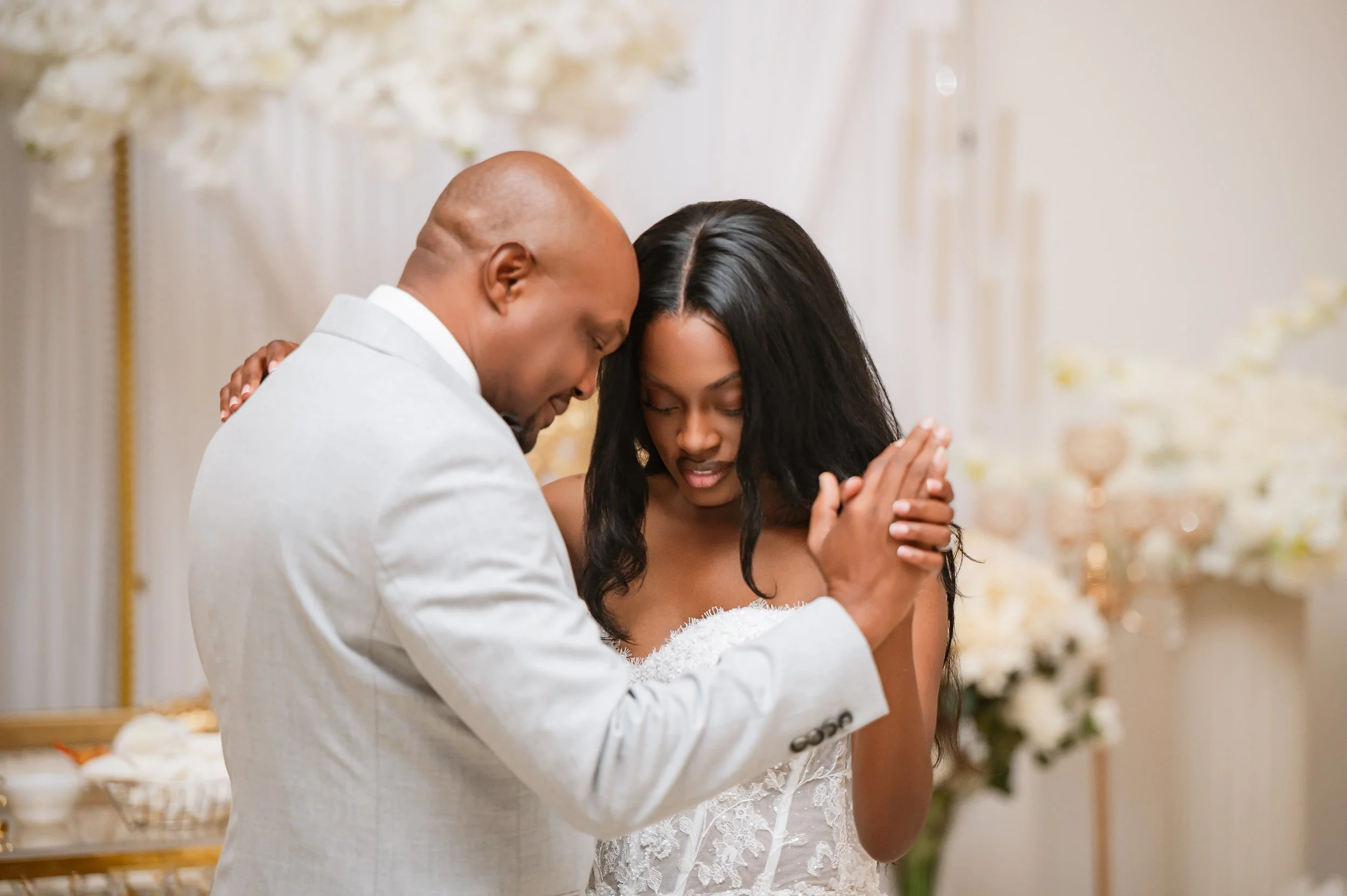 A couple dressed in wedding attire sharing a tender moment and praying together with their foreheads touching.