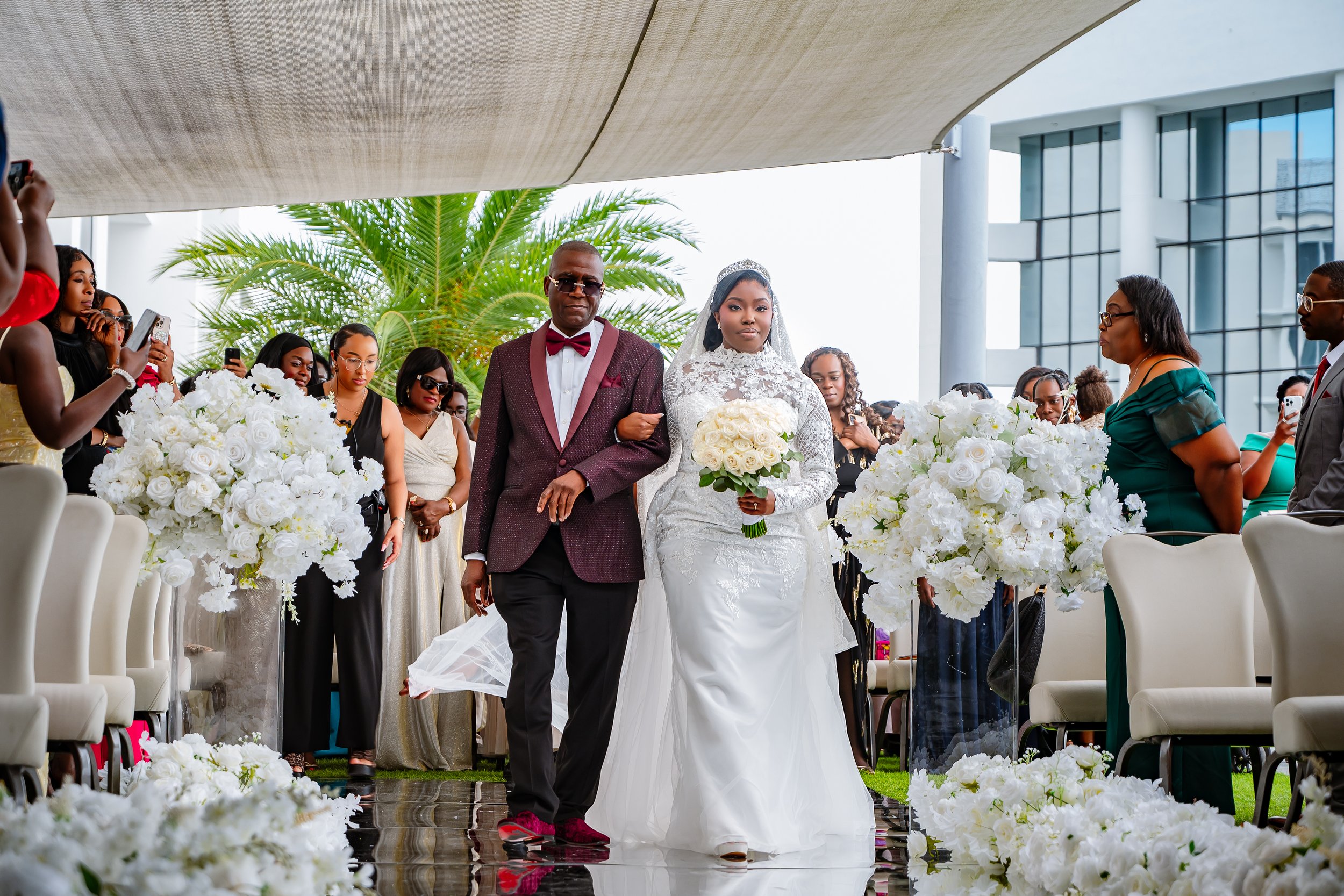 Bride and groom walking down the aisle at a wedding ceremony, surrounded by guests and floral decorations.