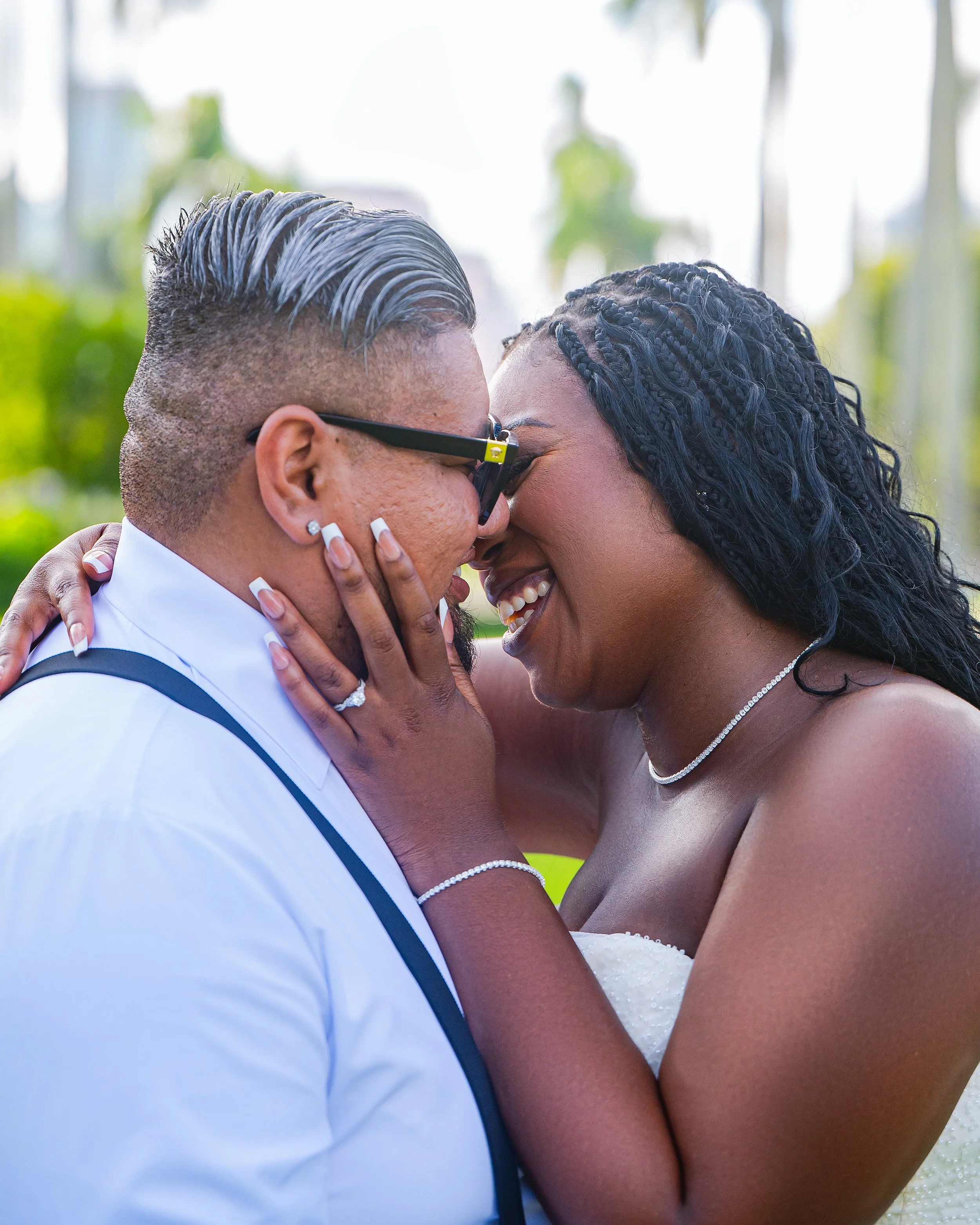 A smiling couple touching foreheads, sharing a joyful moment outdoors during a wedding celebration.