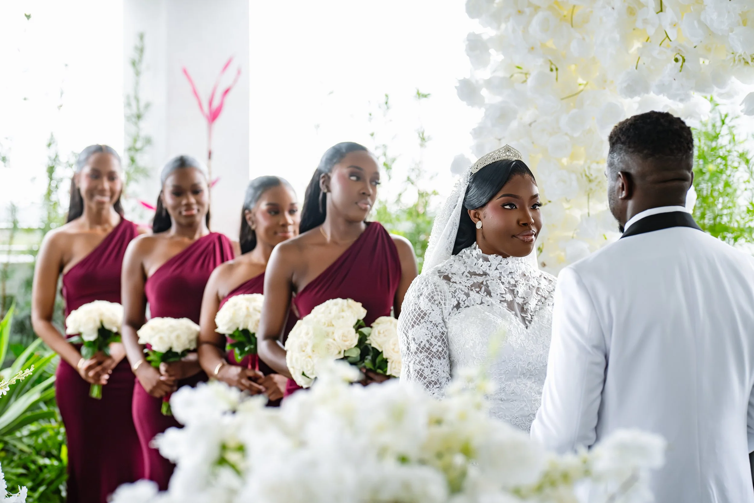 A bride and groom exchange vows during a wedding ceremony, with bridesmaids standing behind the bride holding white bouquets.