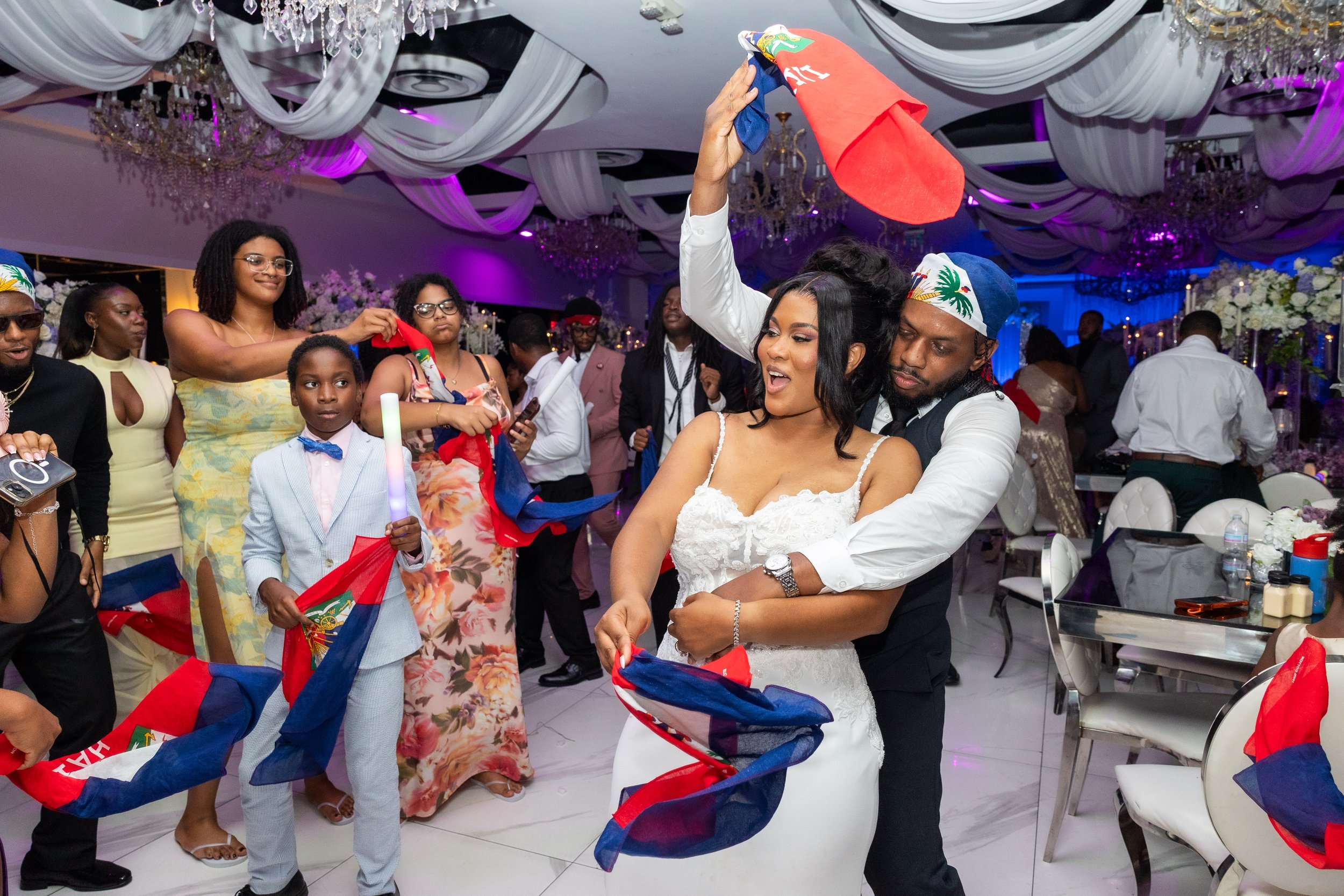 People celebrating at a wedding reception, dancing and holding Haitian flags.