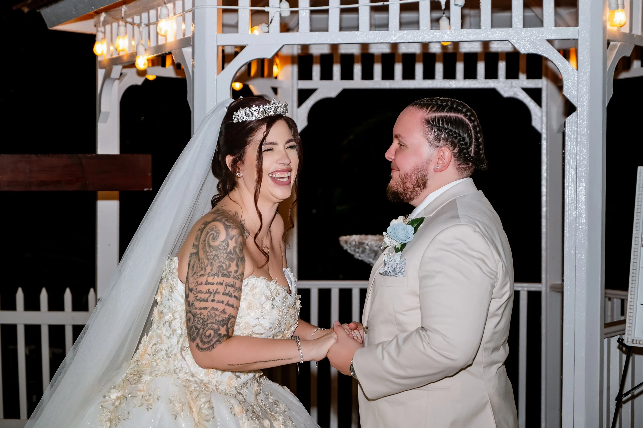 Bride and groom holding hands during their wedding ceremony at night inside a decorated gazebo.
