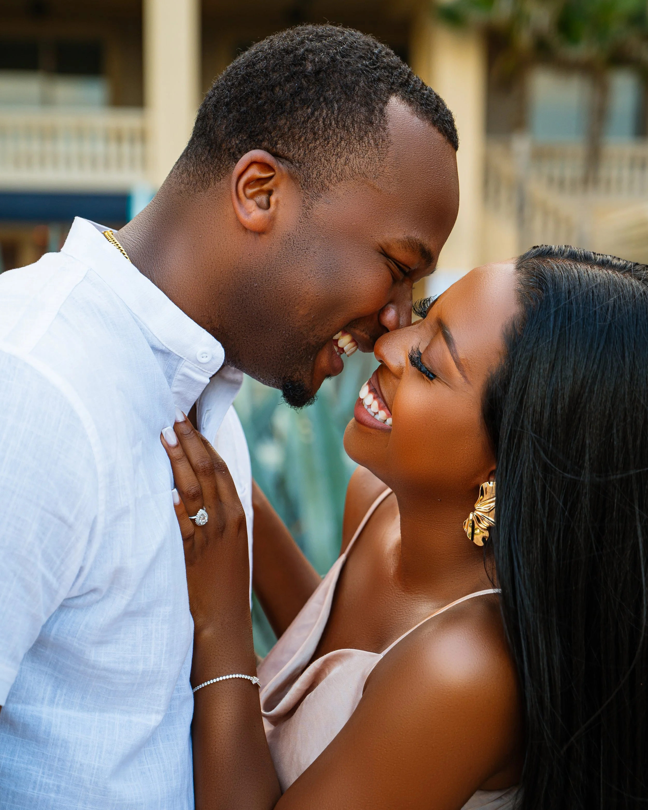 A happy couple smiling and leaning close together outdoors, with their foreheads touching and eyes closed, showing affection.
