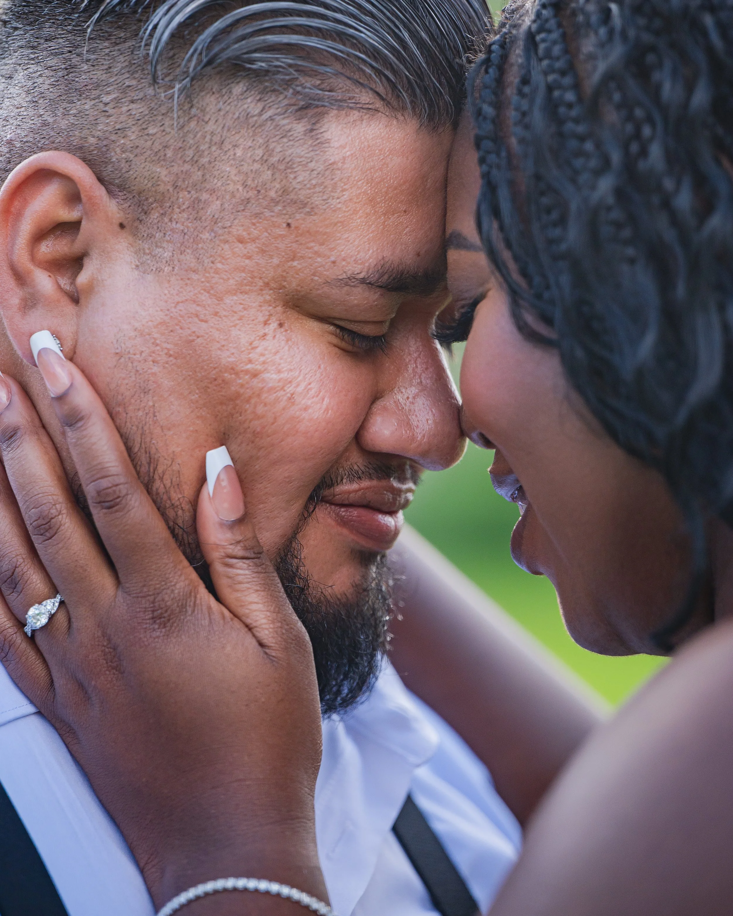 A couple sharing an intimate moment with their foreheads and noses touching, eyes closed, and smiling gently.