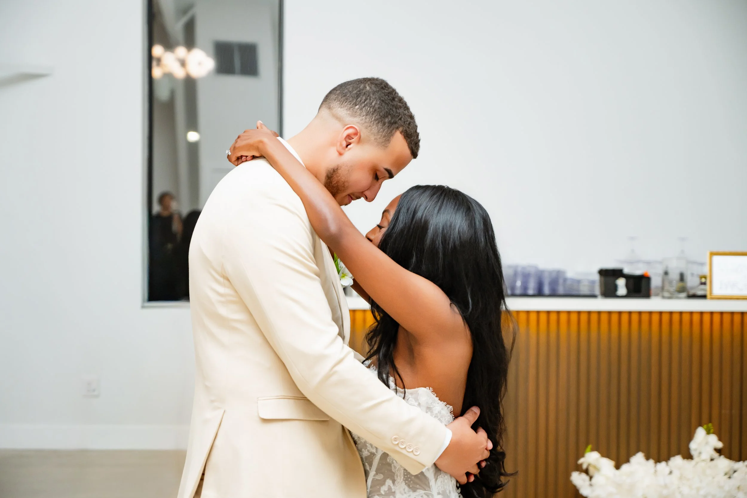 A couple in wedding attire embracing each other in a dance or hug at a wedding reception.