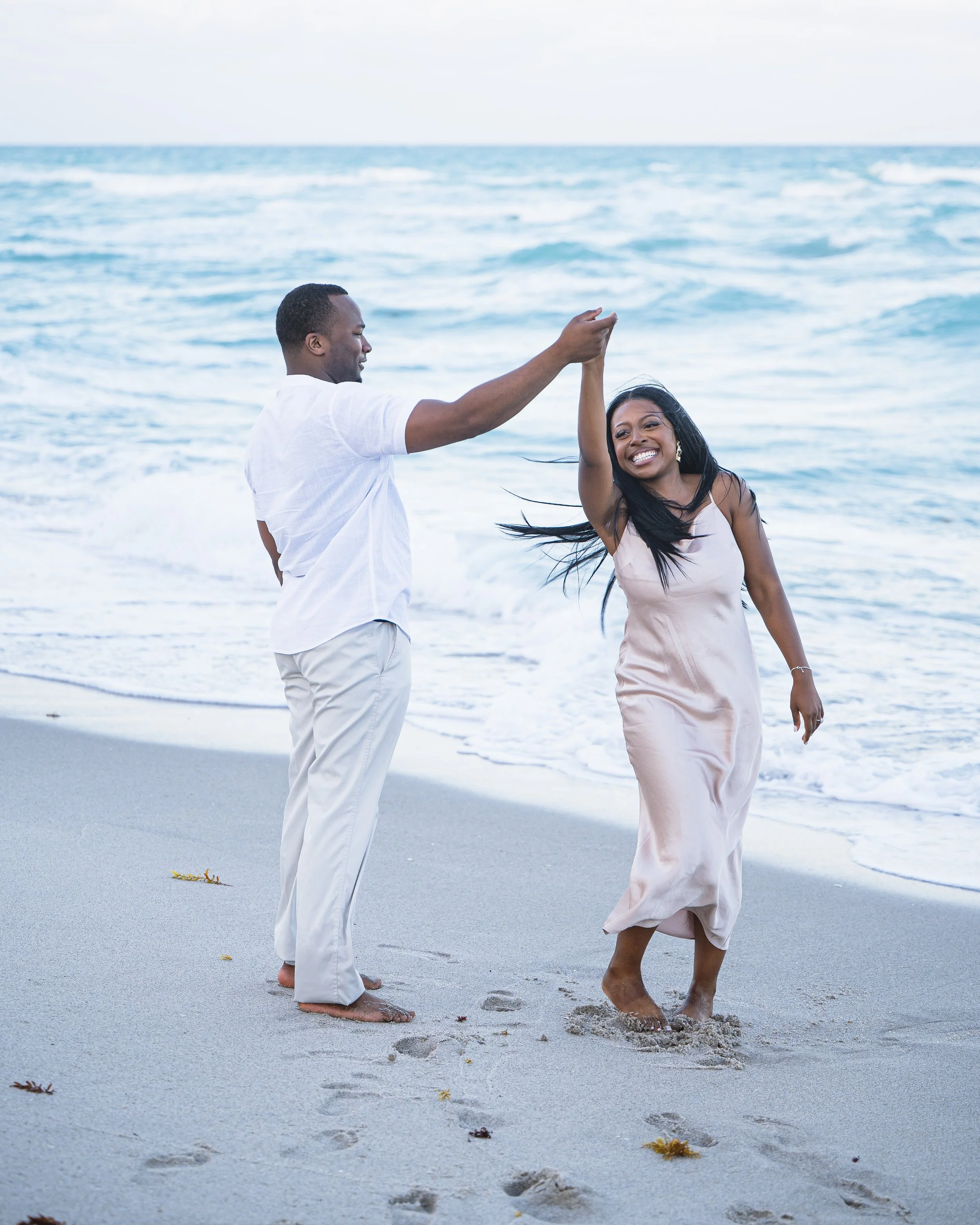 A couple dancing on the beach near the ocean, smiling and enjoying the moment.