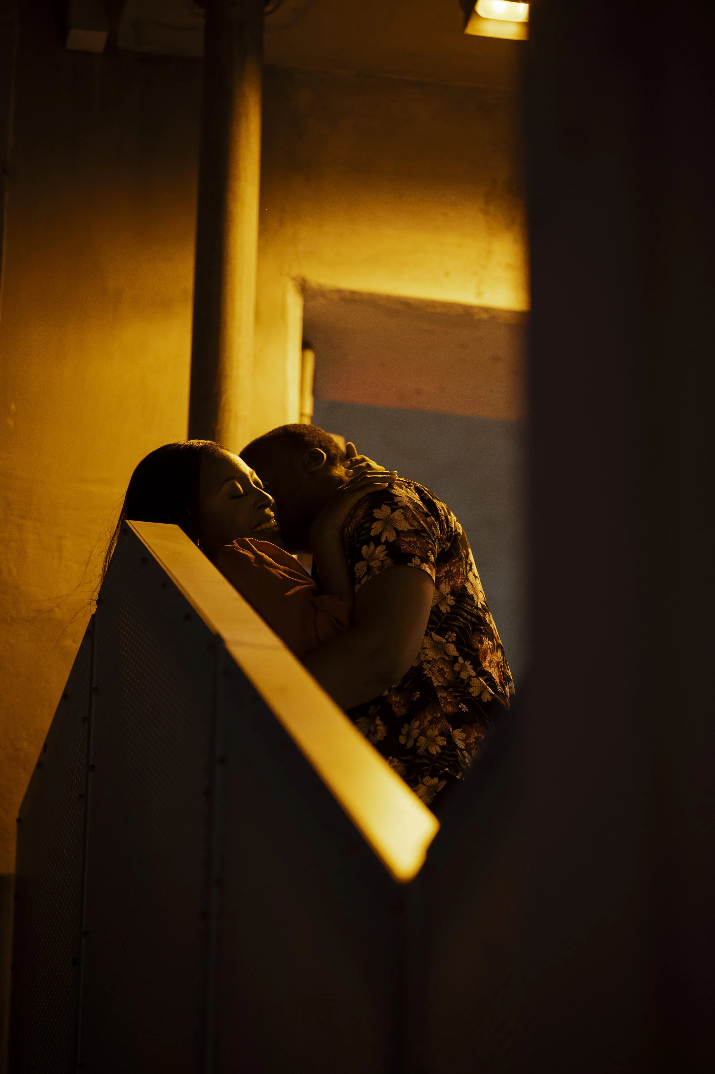 A couple embraces on a balcony at night, with warm lighting illuminating their faces.
