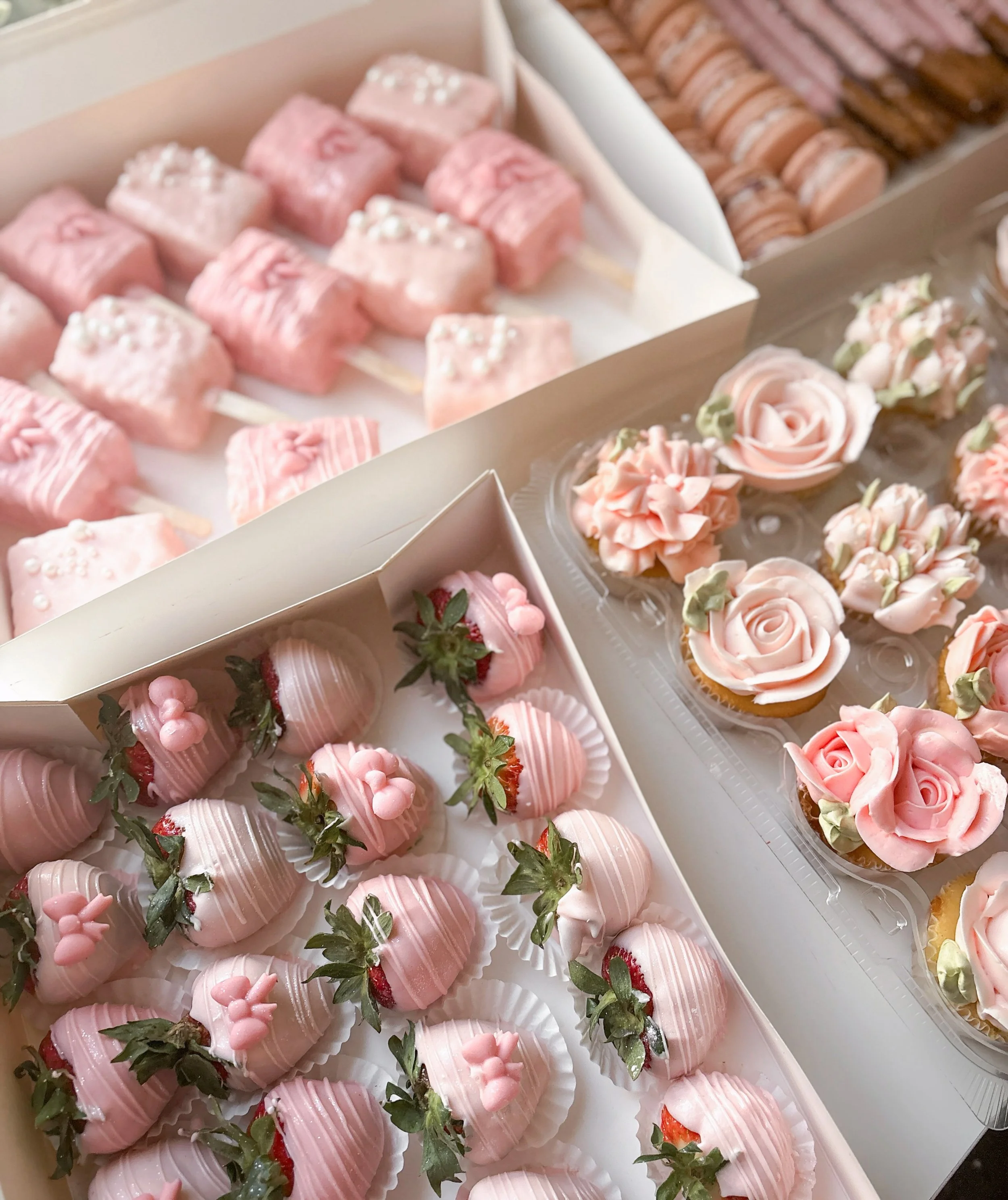 Assorted pink desserts including strawberry-covered chocolates, pink rose-shaped cupcakes, and strawberry-flavored marshmallows with pastel decorations.
