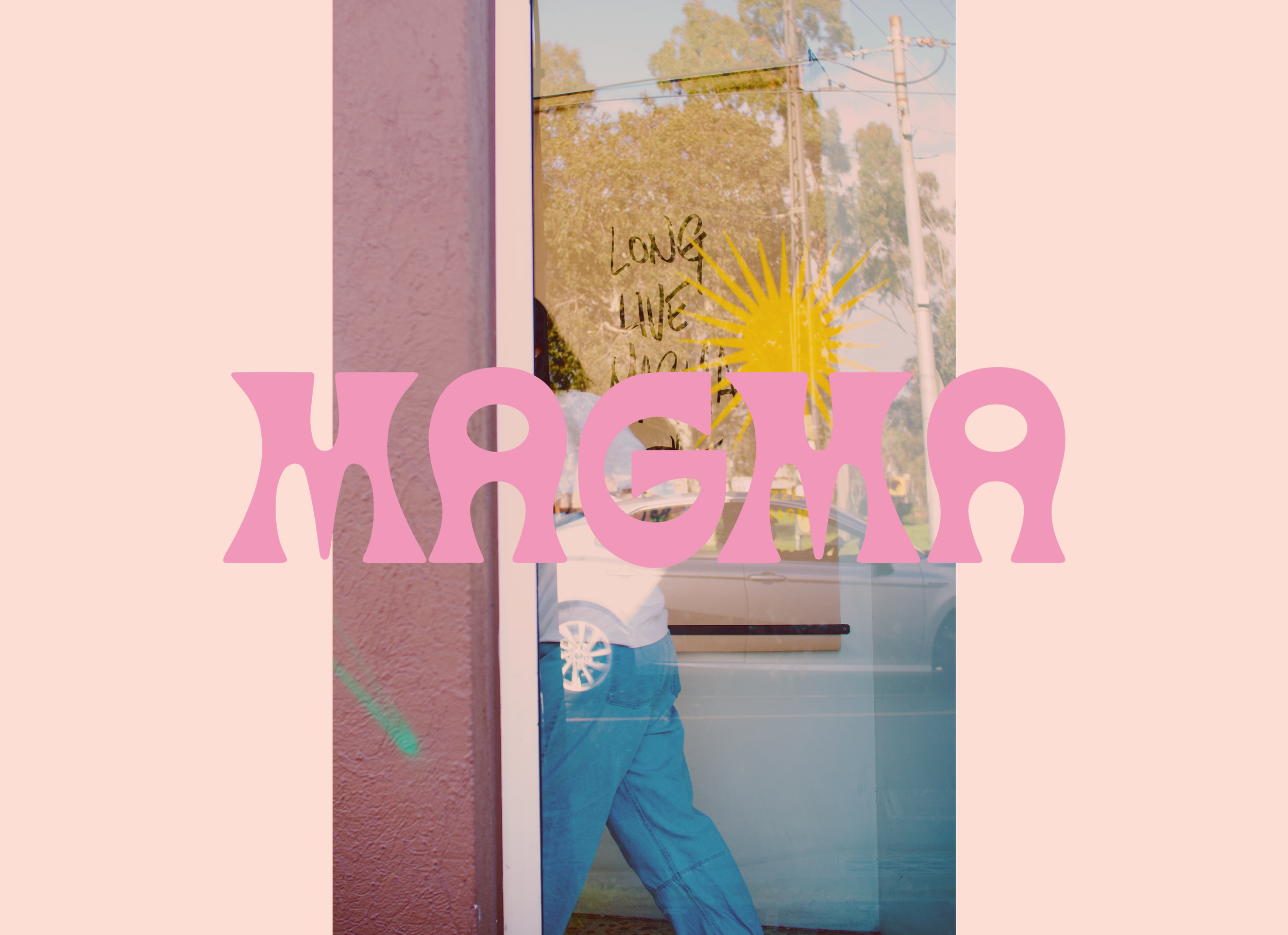 A person is standing inside a storefront with glass windows, with their reflection visible in the glass. The person is wearing a blue shirt and jeans, and the wall in the background reads "Love Live Magma"