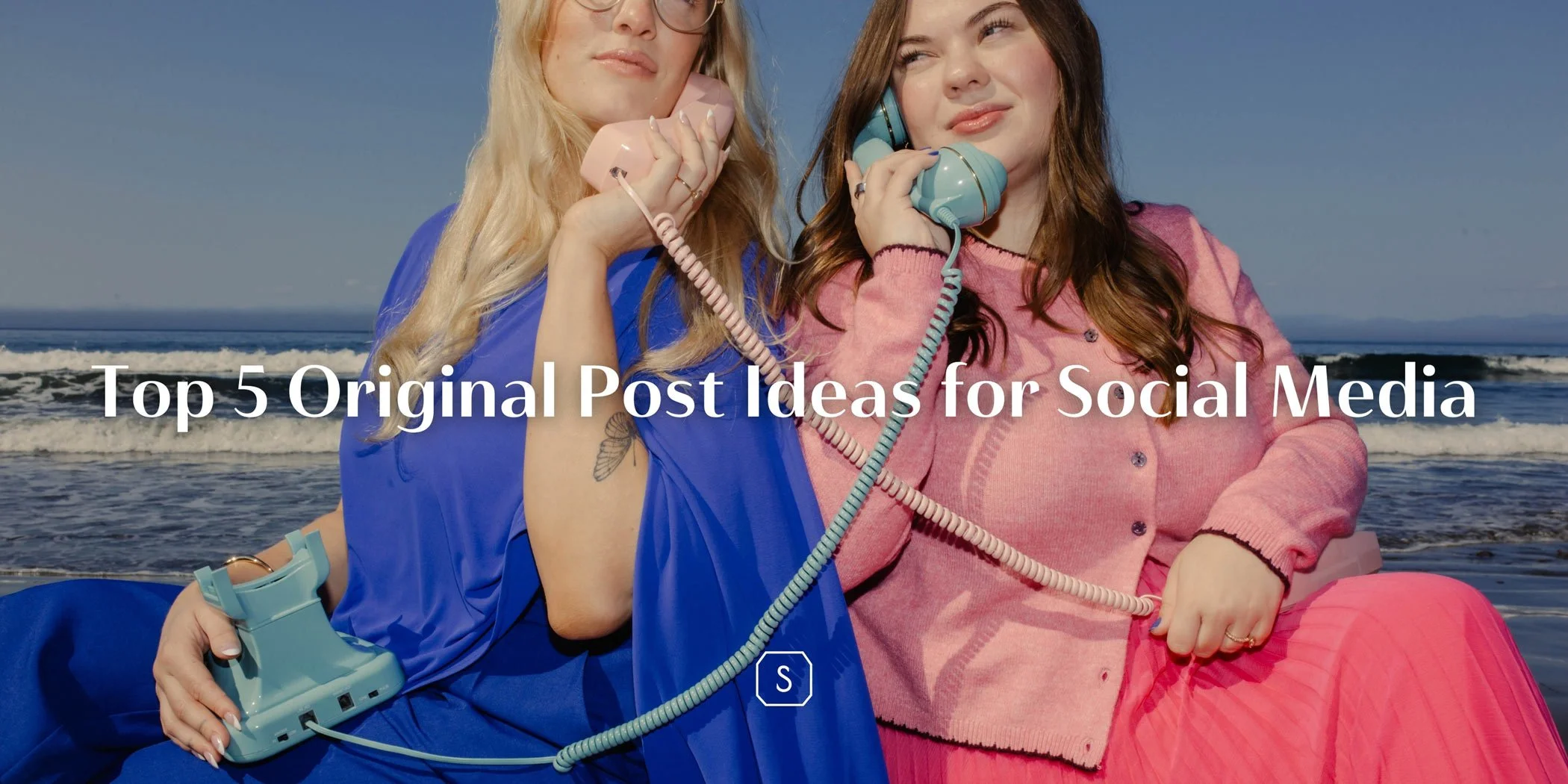 Two women sitting in front of the ocean holding vintage phones to their ears while wearing blue and pink business clothes
