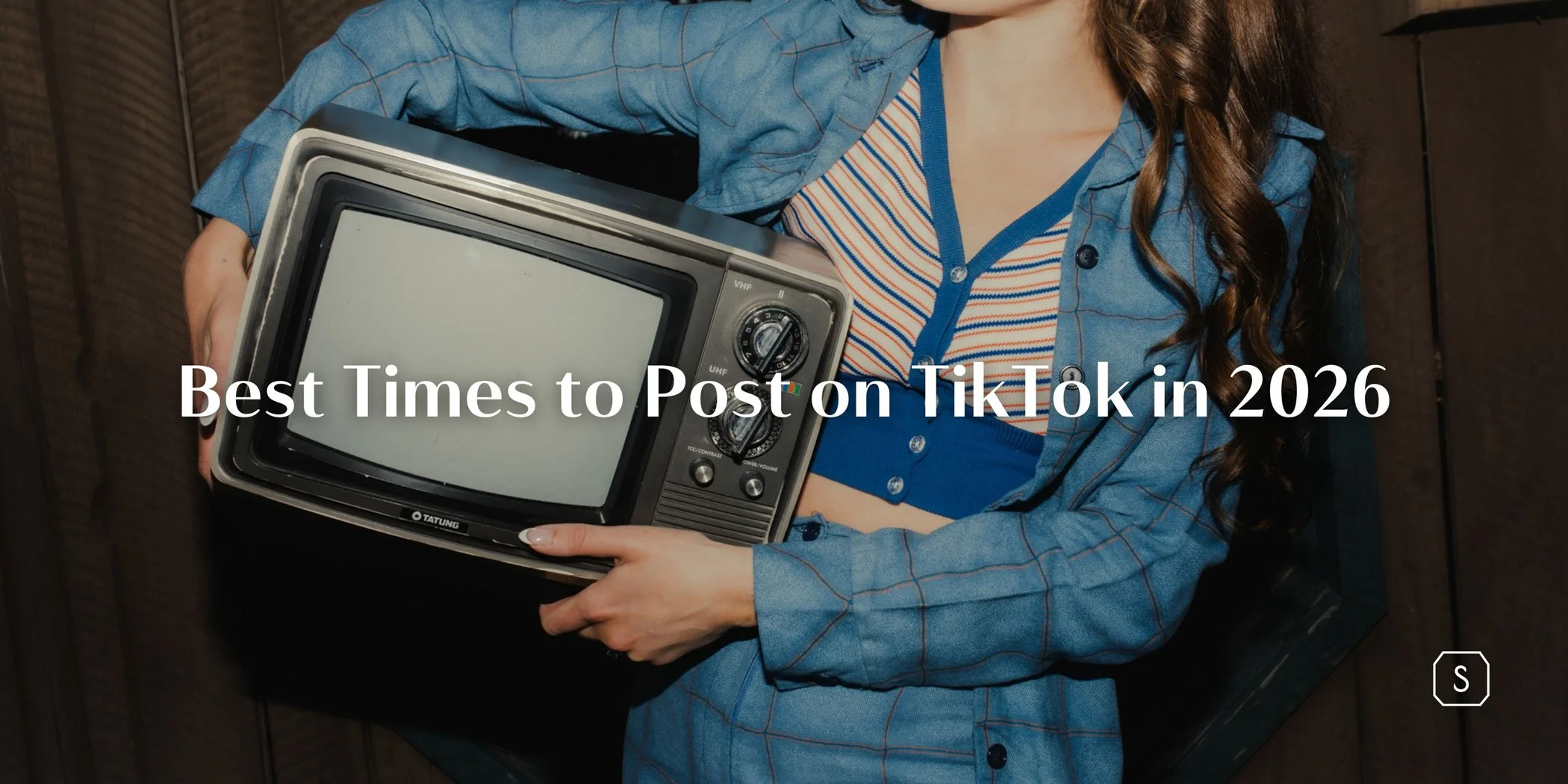 woman in a blue suit and striped top holding a vintage television under her arm