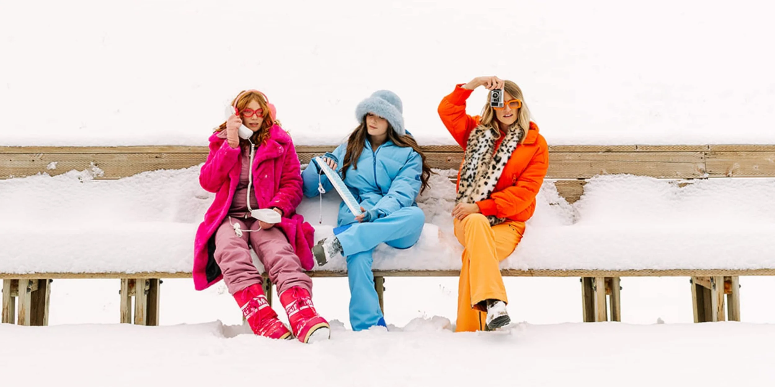 Content Calendar Asana: Three women posing on a bench with winter gear in the snow holding electronics