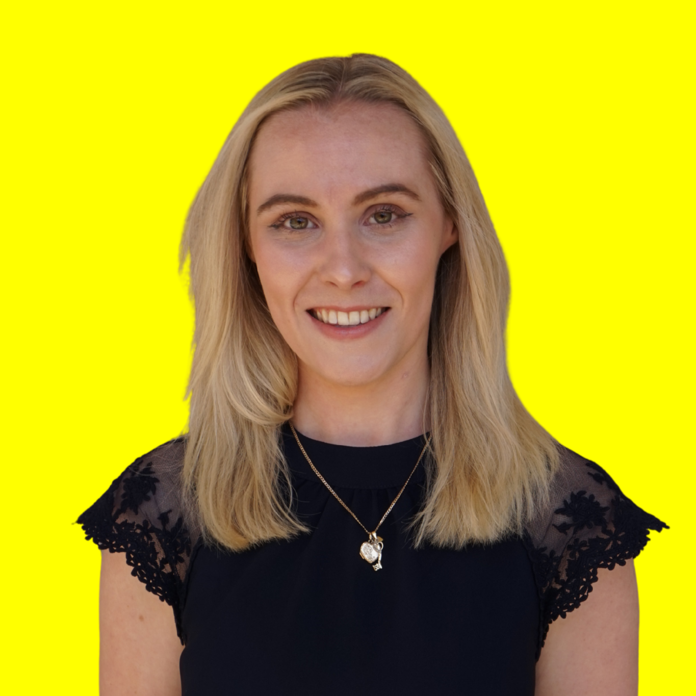 A smiling young woman with blonde hair wearing a black top with lace sleeves and a gold necklace with a heart pendant, standing against a bright yellow background.