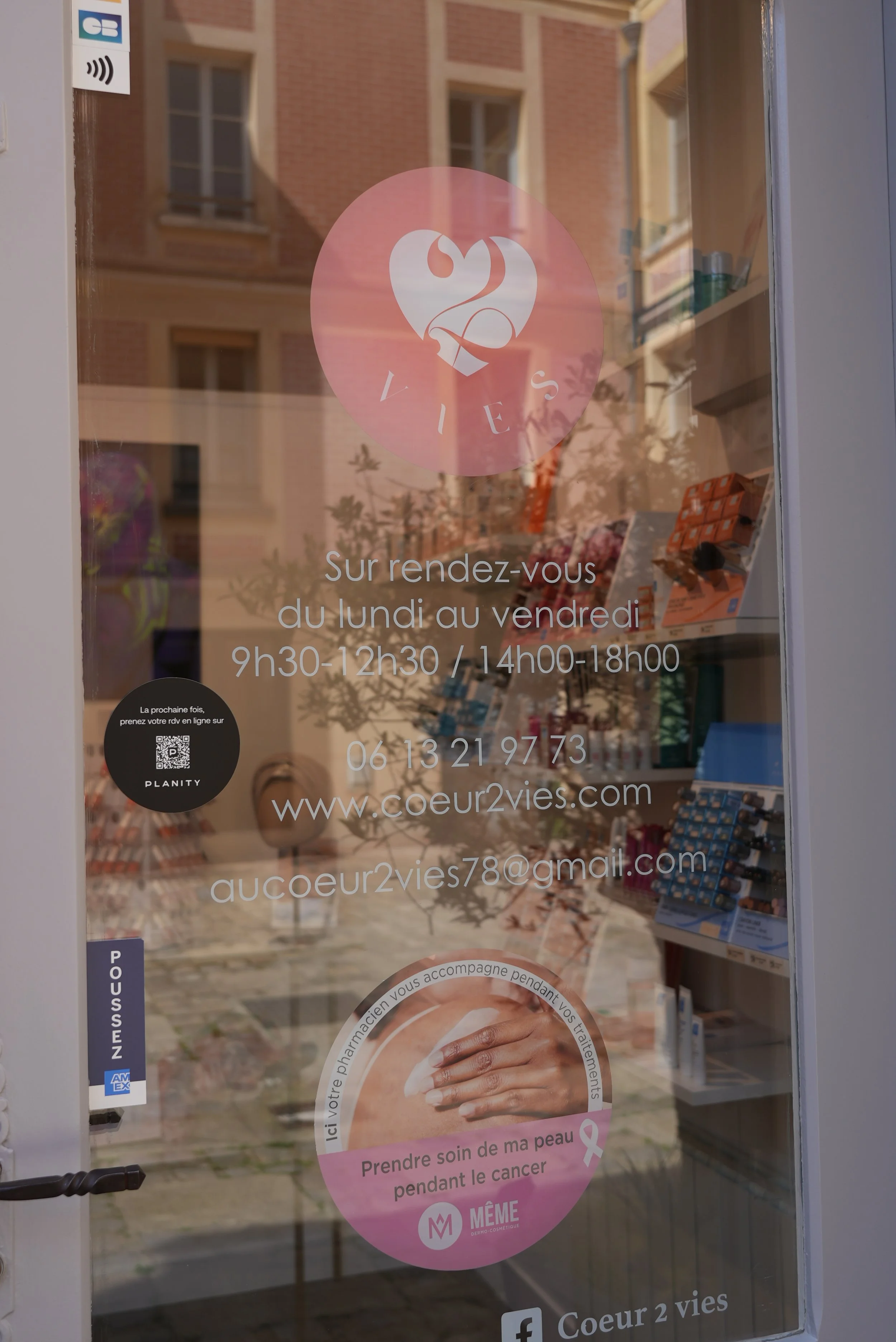 L'enseigne d'un salon de beauté ou clinique de soins, avec des heures d'ouverture, un numéro de téléphone et une adresse web. Il y a aussi un logo avec deux coeurs stylisés et un ruban rose, symbole de la lutte contre le cancer du sein.