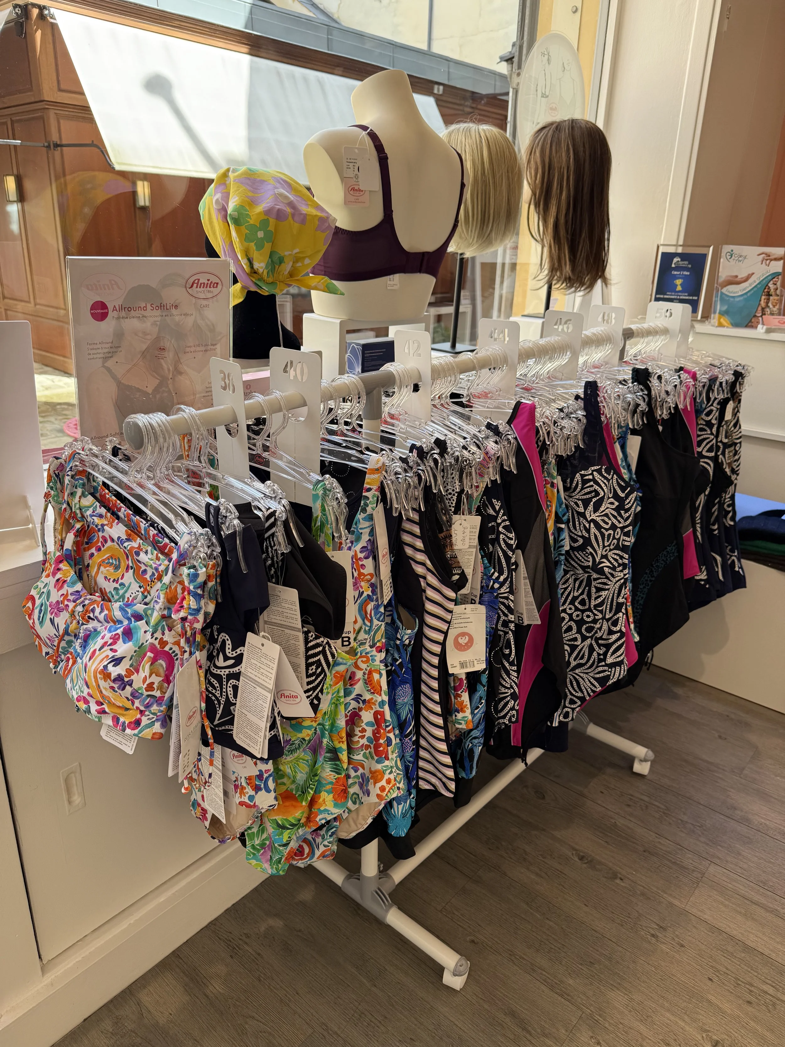 Vitrine exposant des maillots de bain pour femmes, avec des mannequins et des étiquettes de prix, dans un magasin proche d'une fenêtre