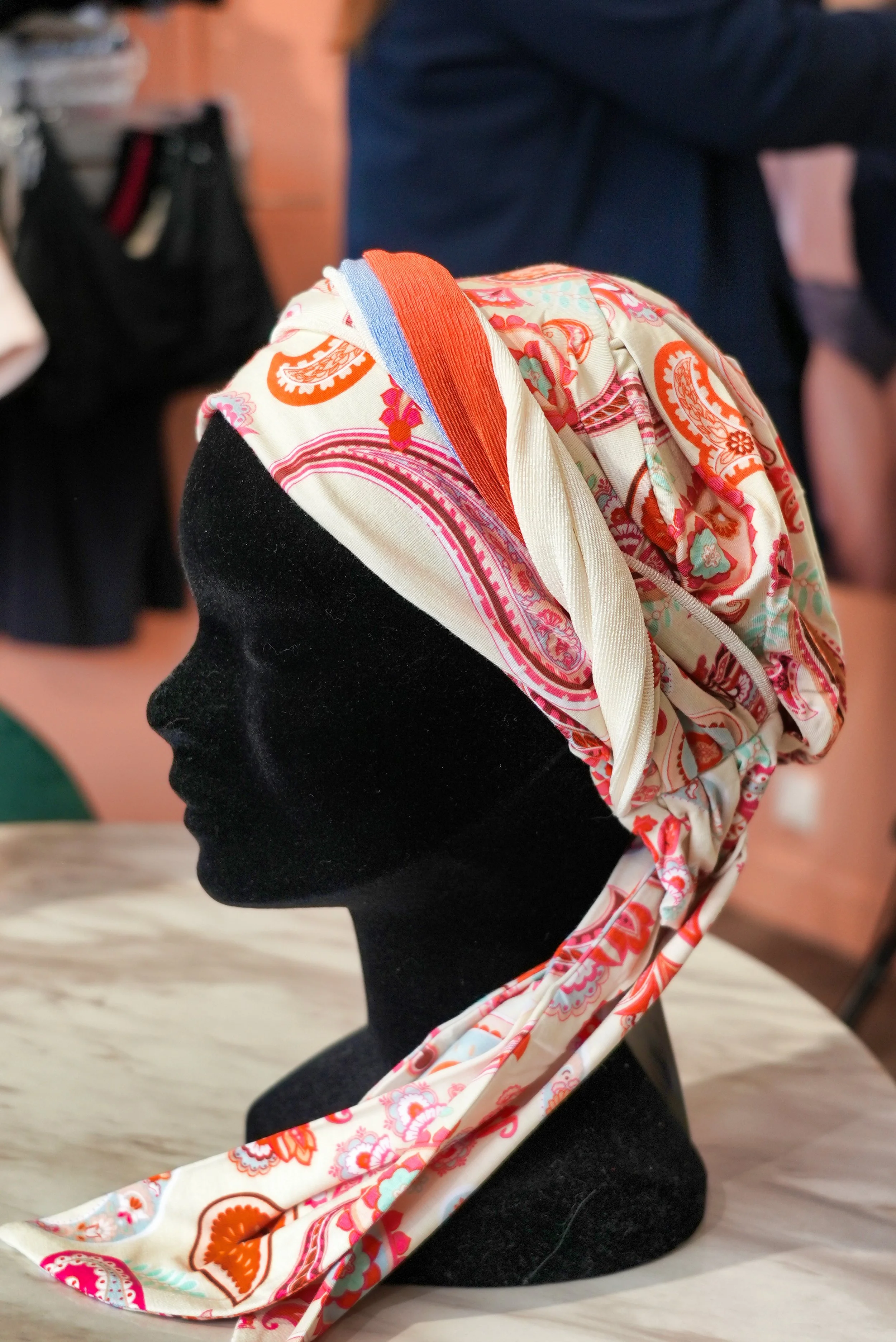 Un mannequin en velours noir portant un foulard coloré avec des motifs floraux et géométriques, attaché autour de la tête.