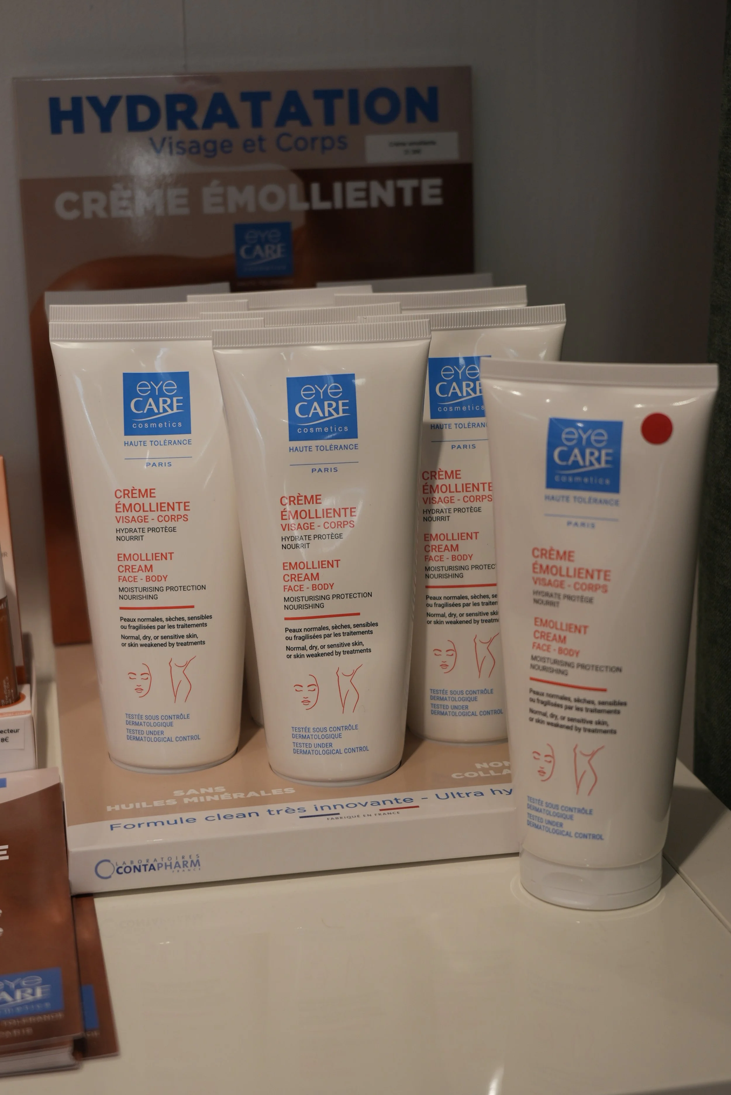 Display de crème émolliente pour visage et corps, en tubes blancs avec logo blue care, sur un étalage en pharmacie.