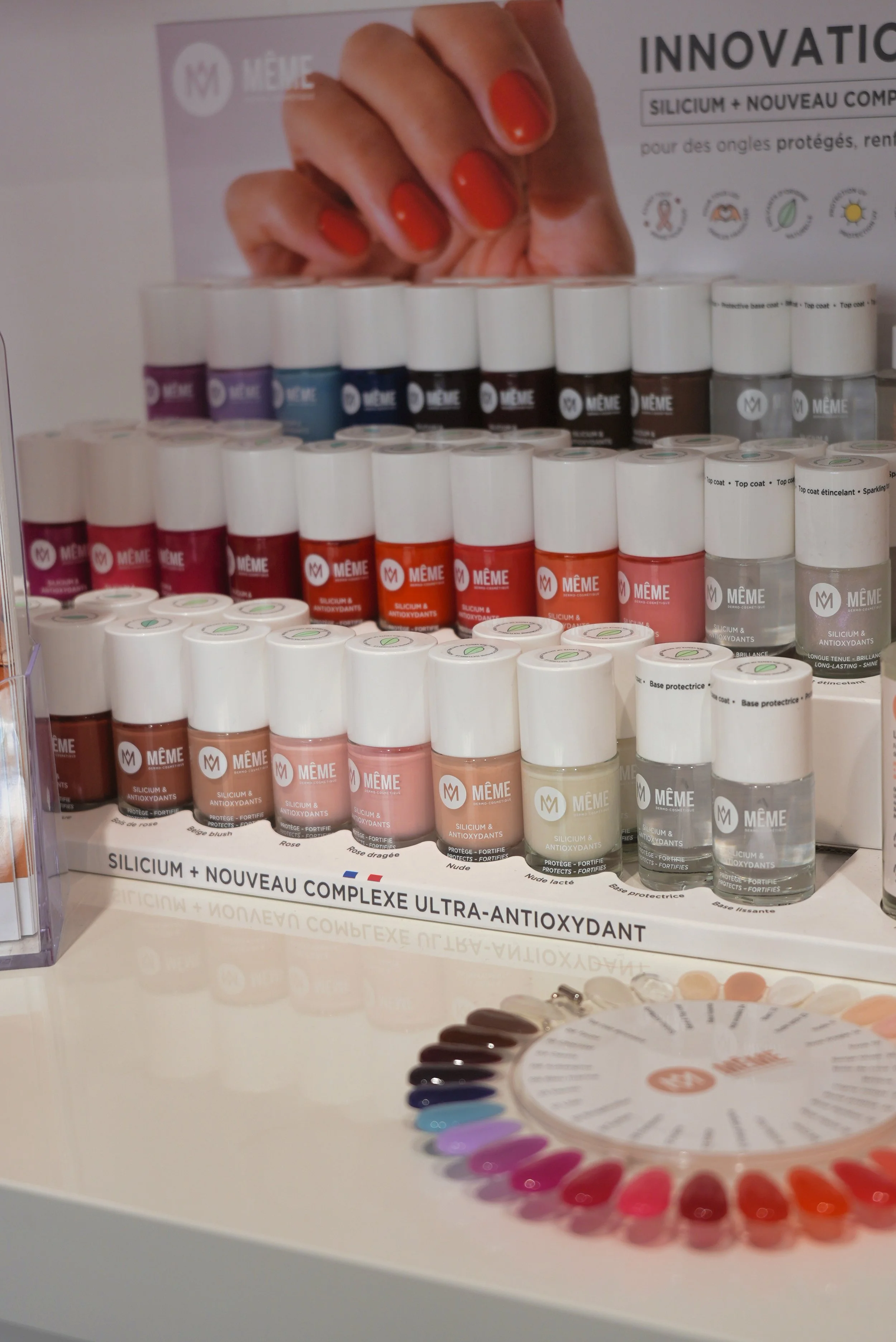 Présentation de produits cosmétiques en vernis à ongles colorés, avec un échantillonneur de couleurs en cercle, et des flacons de vernis à ongles dans différentes couleurs, sur un fond de panneau promotionnel.