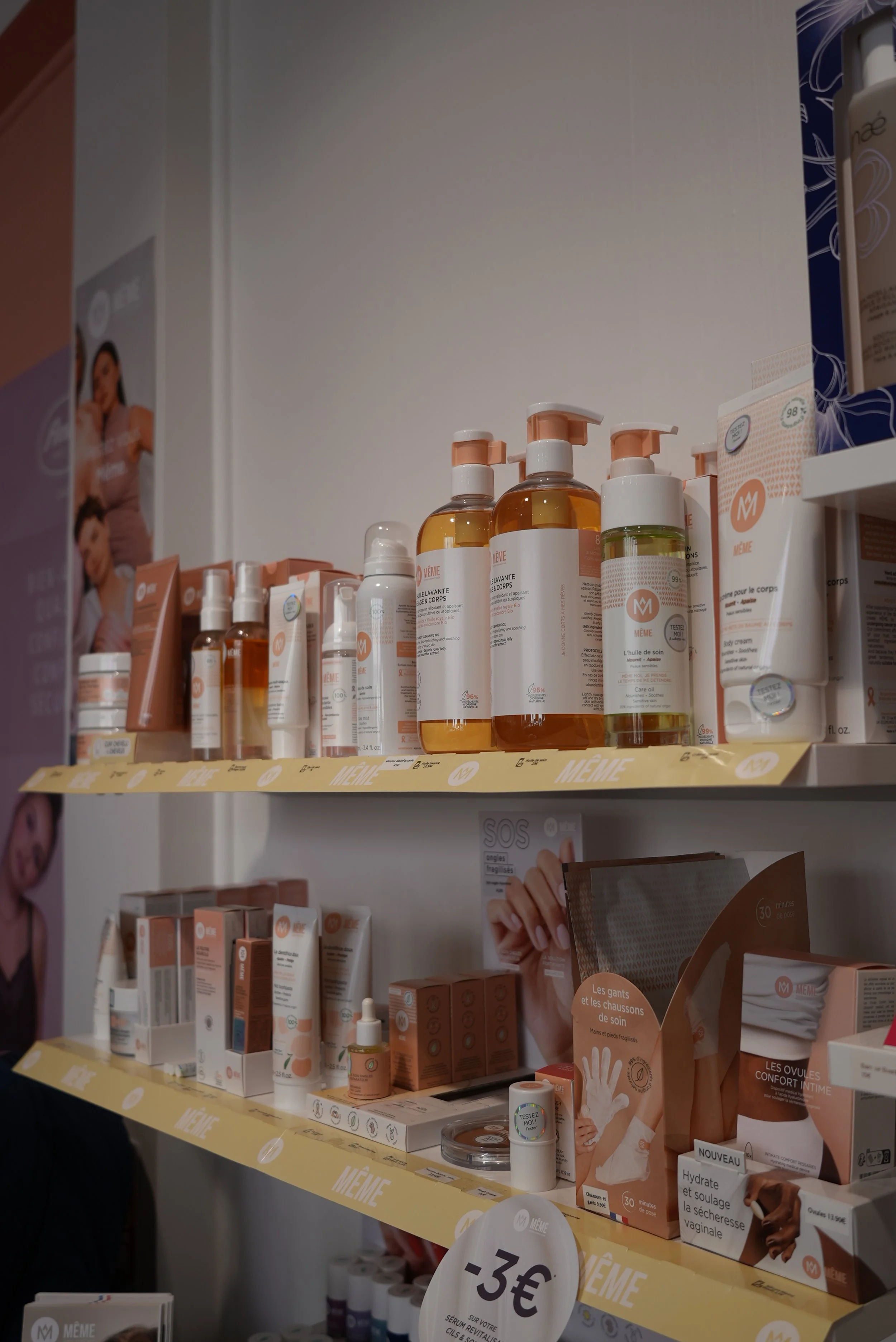 Étals de produits de soins et de beauté dans un magasin, comprenant des bouteilles, des tubes, et des brochures promotionnelles, avec une signalisation indiquant un prix de 3 euros.