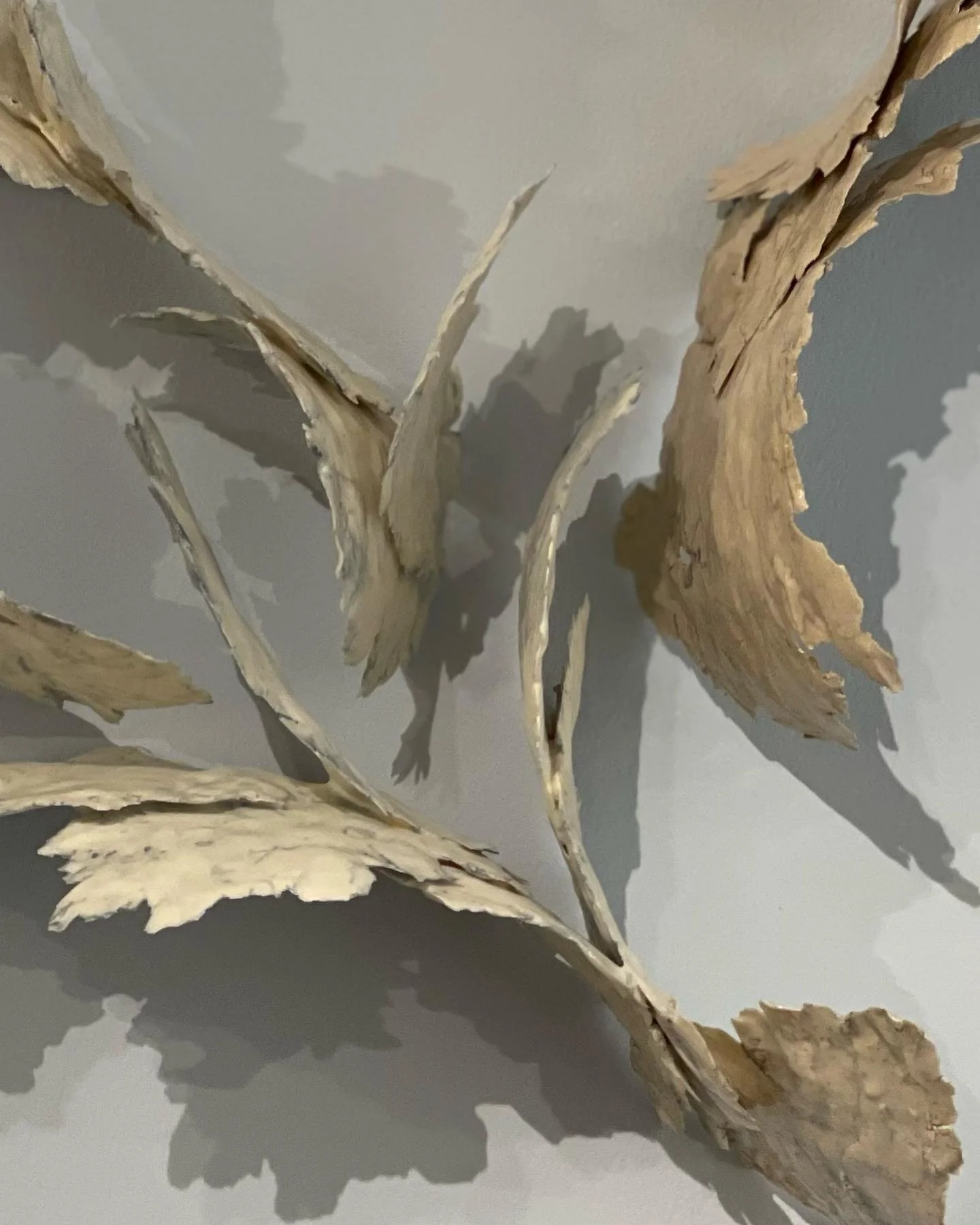 Abstract wall sculpture with curved, textured beige metal sheets.