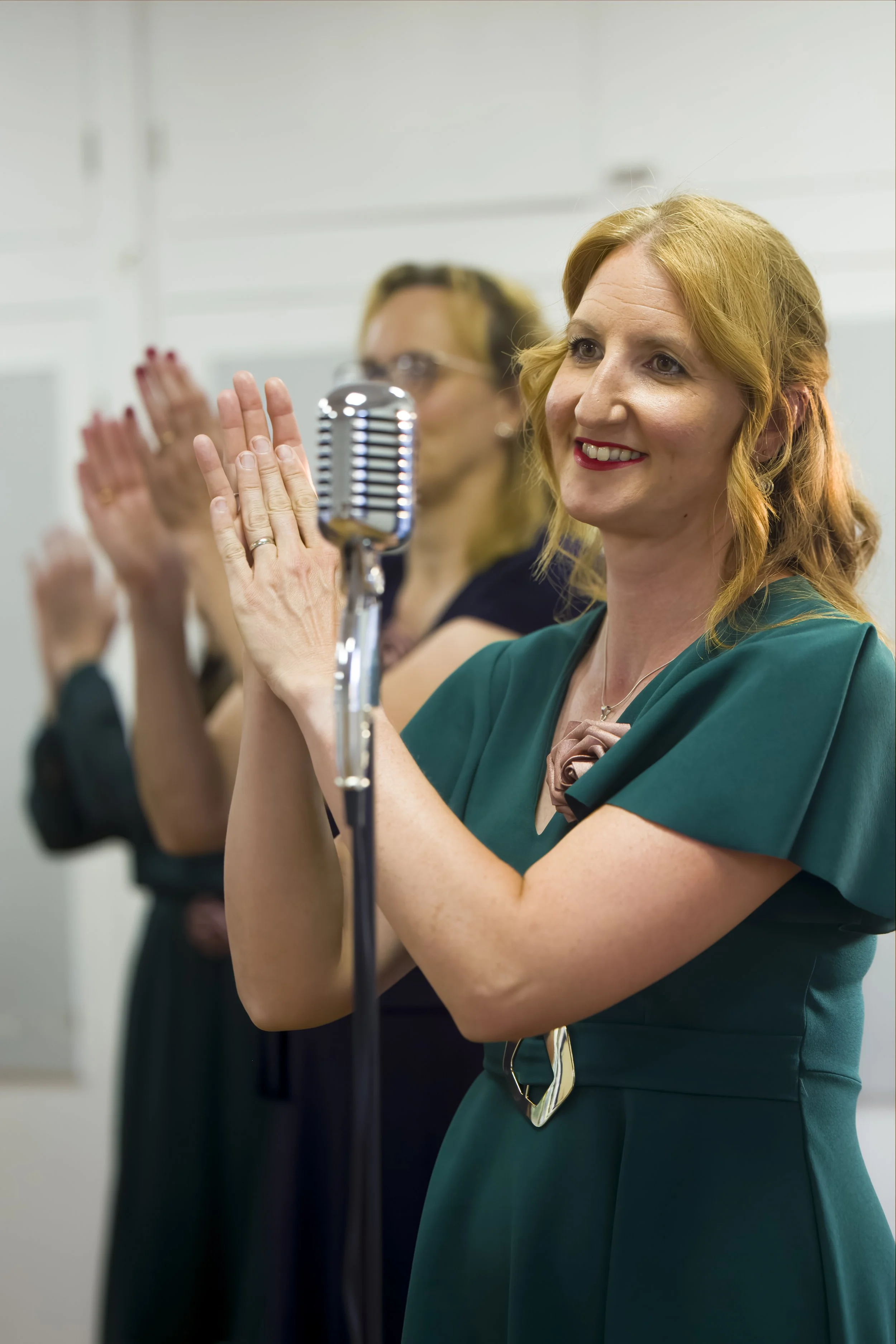 Women from The Fifty choir clapping as part of choreographed movement during a performance in Southend-on-Sea with a vintage microphone in the foreground.