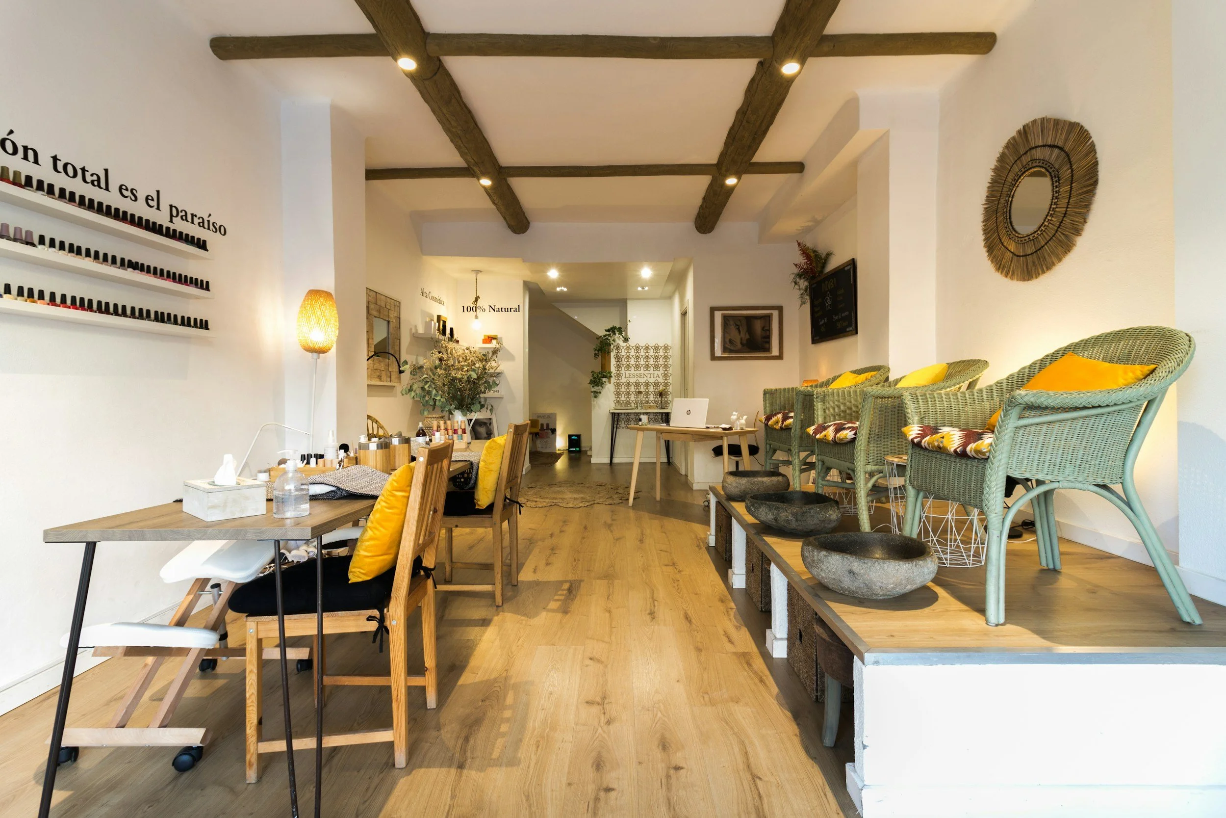 Interior of a nail salon with seating and nail polish display, wooden beams on ceiling, and decorative mirrors on white walls.