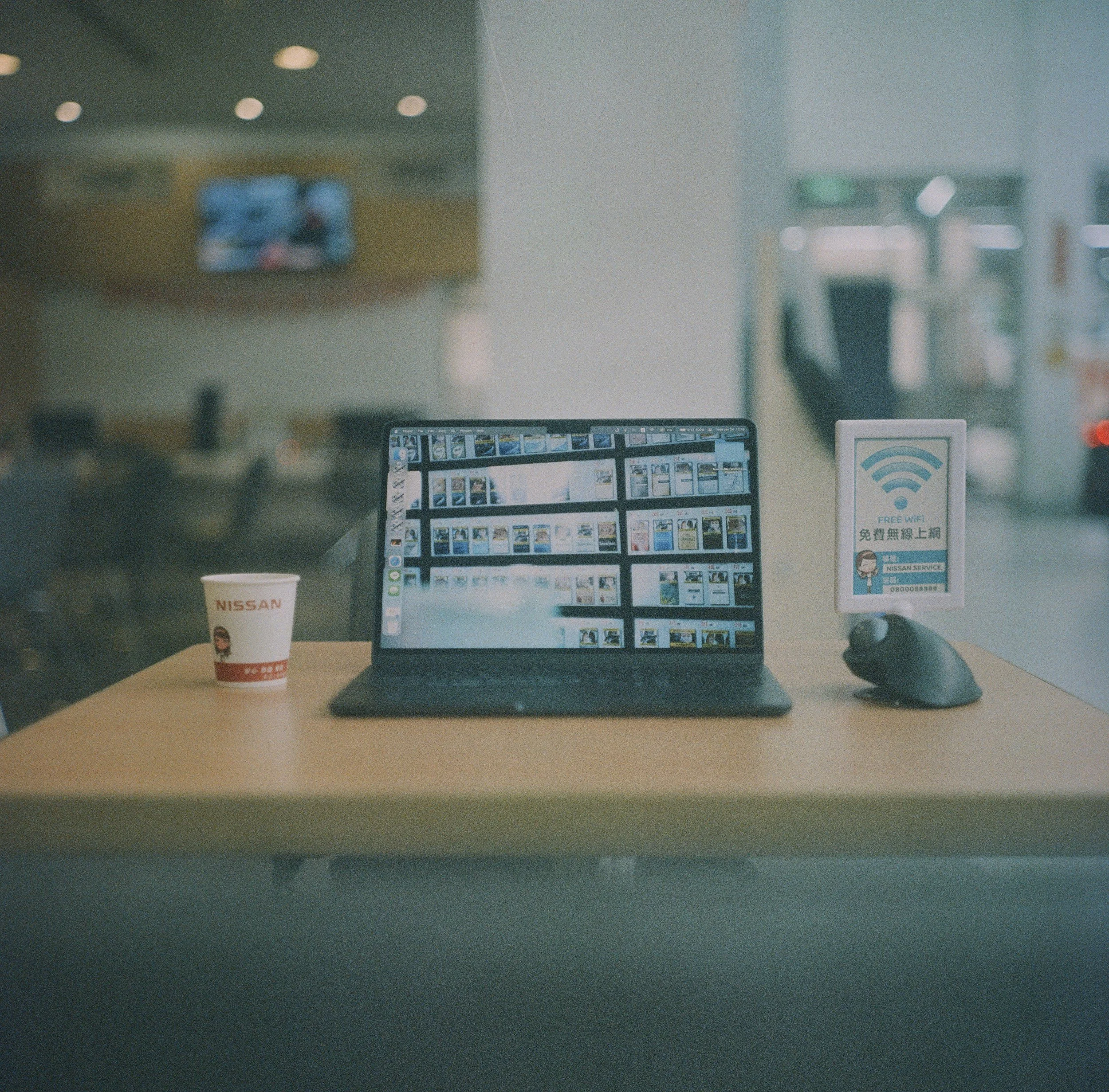 A computer monitor displaying image thumbnails in a store or office setting, with a sign indicating free WiFi and a cup labeled Nissan on the desk.