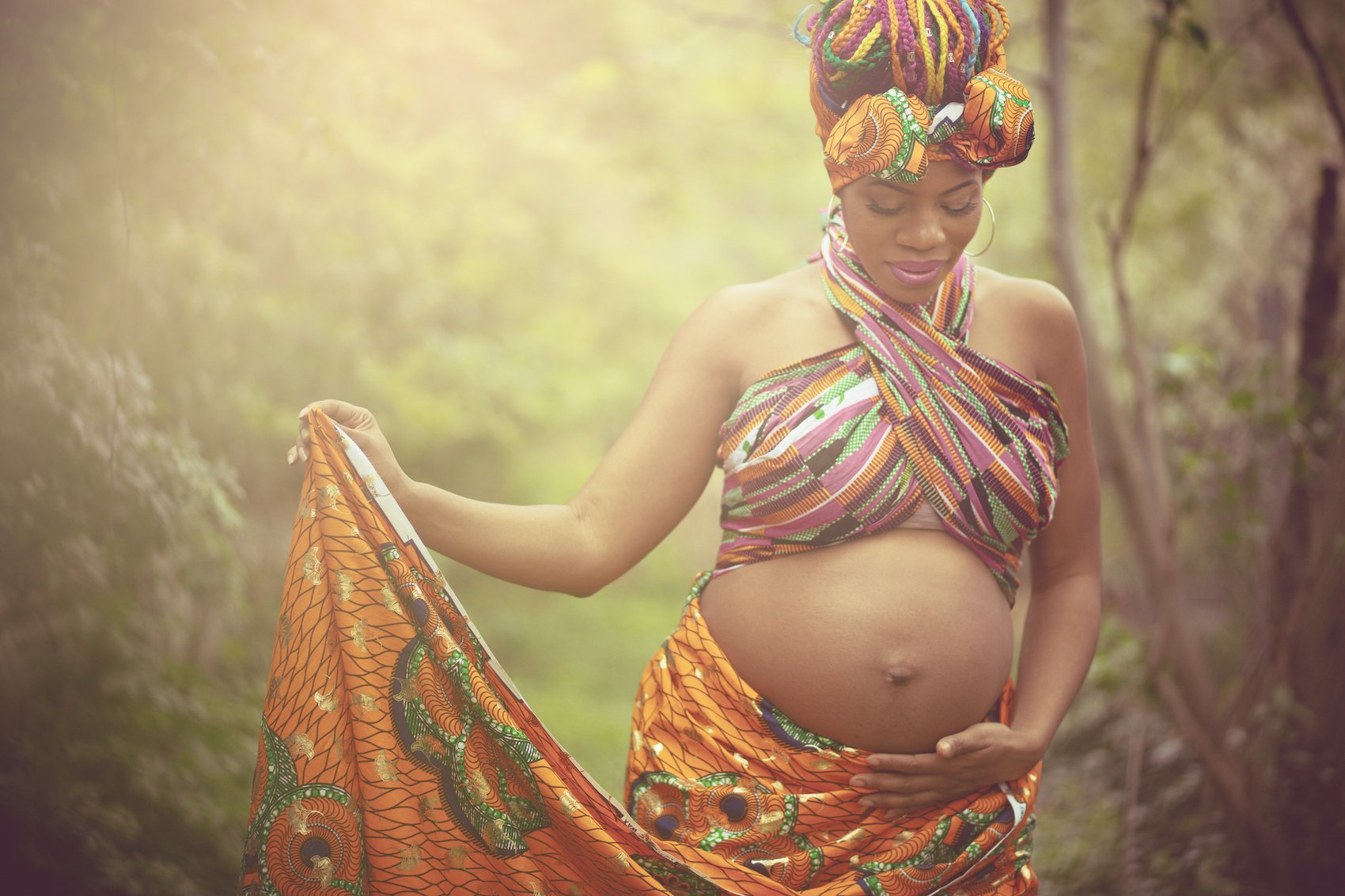 African pregnant woman dressed in beautiful traditional garments makes her way through the countryside. She seems relaxed, and confident.