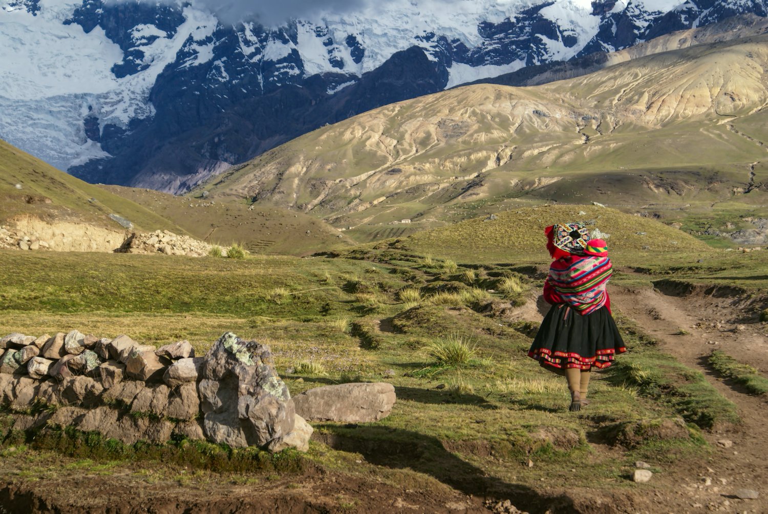 Young Peruvian Mama makes her way across the remote landscape of the Altiplano. She's dressed in traditional costume and her baby is attached to her back in colourful woven cloth