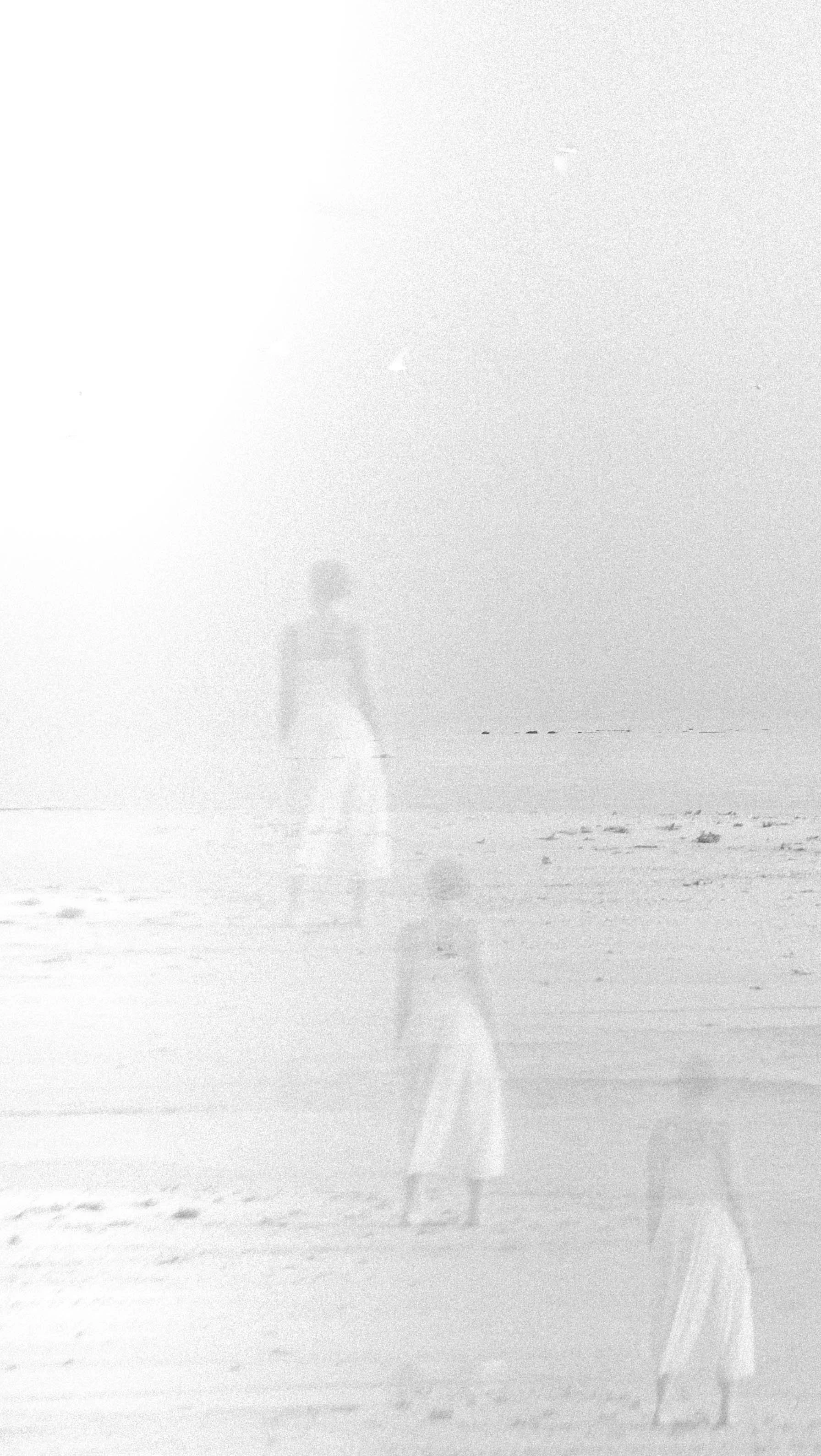 A double exposure photograph of women walking on the beach with the ocean in the background. The image appears to have a ghostly, transparent effect.