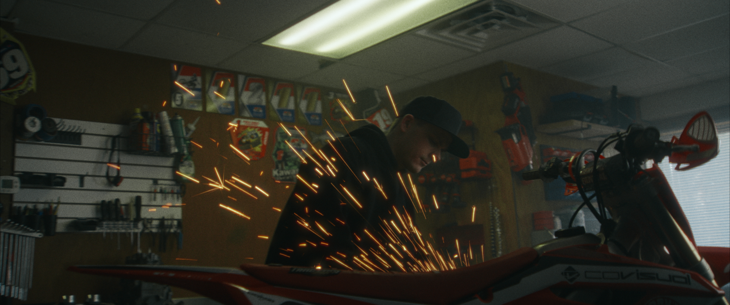 A man welding on a red dirt bike in a workshop, sparks flying.