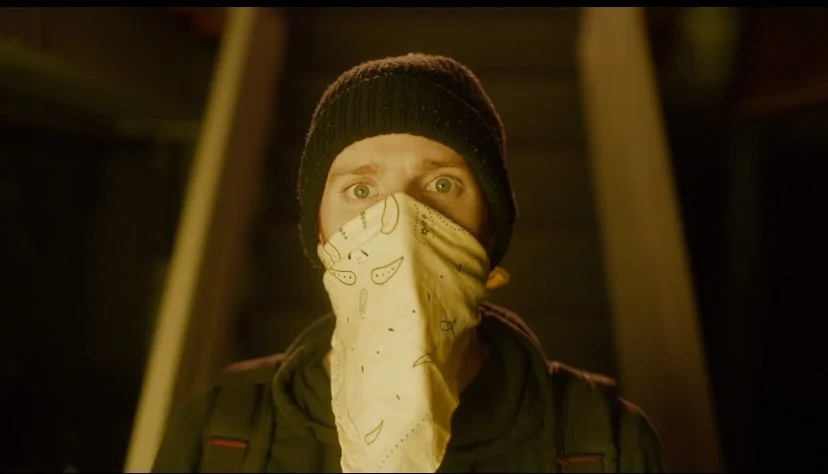 A person wearing a black beanie, a bandana covering their nose and mouth, and a dark jacket.