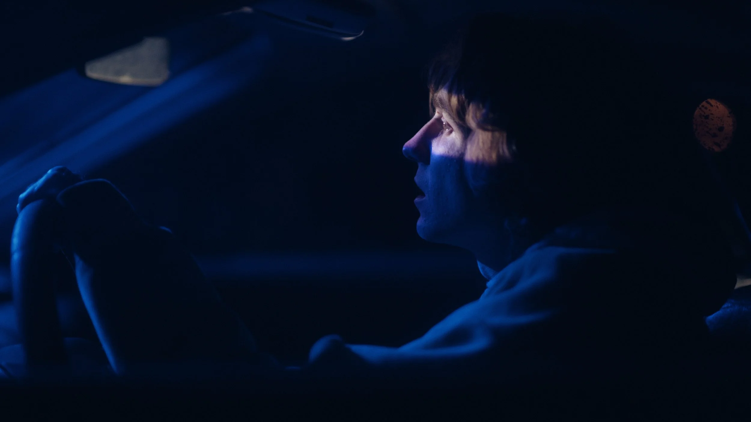 A person driving a car at night, illuminated by a blue light from the dashboard, with their hands on the steering wheel and a focused expression.