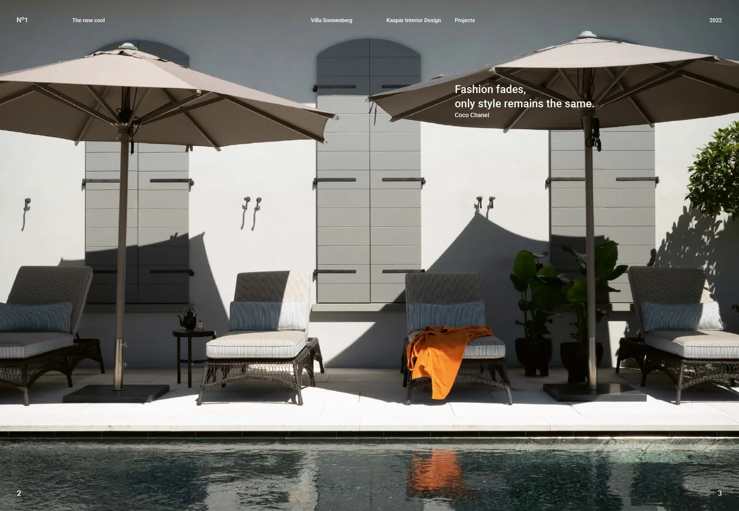 Poolside view with four lounge chairs, two large umbrellas, a small black side table, green potted plants, and a white wall with gray shutters in the background.