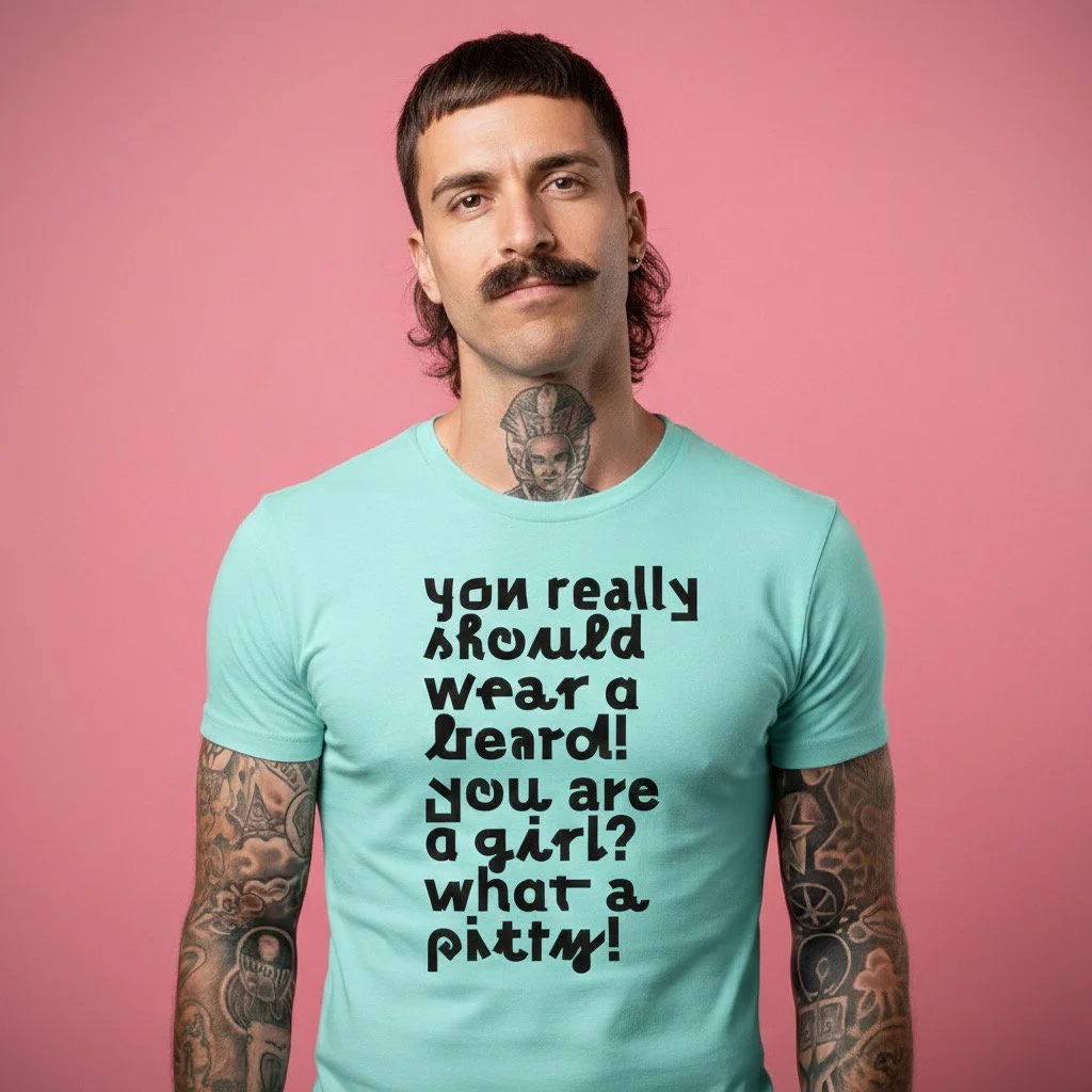 A man with a mustache, tattoos on his arms, and a tattoo on his neck, wearing a light blue T-shirt with bold black text. The background is pink.